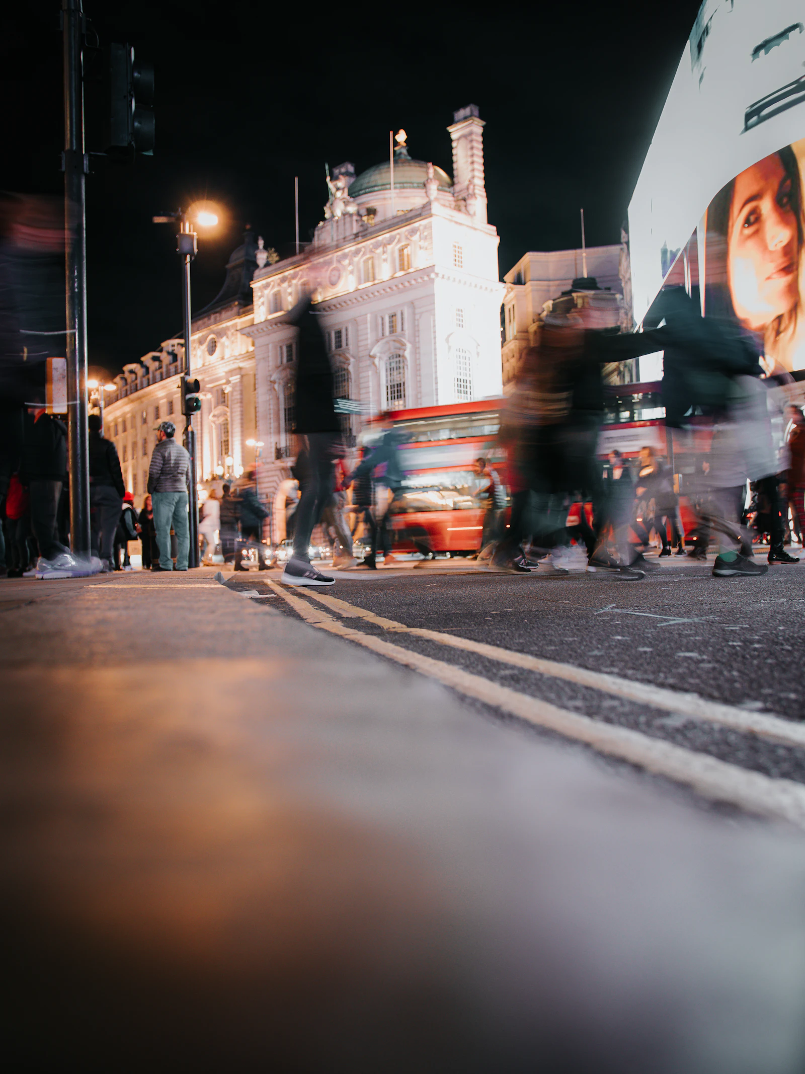 People crossing a city street at night near a bus, in motion blur
