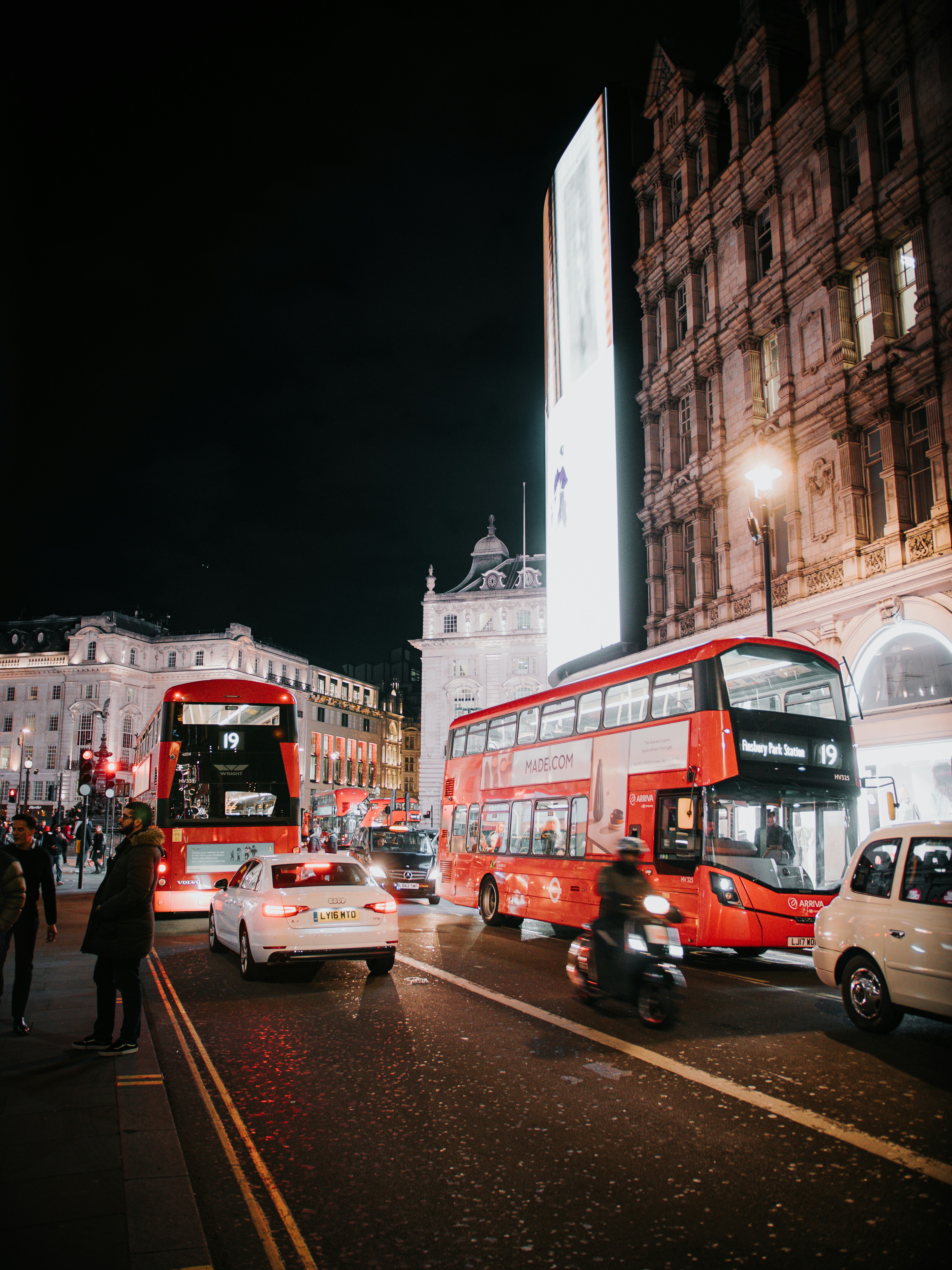 Red double-decker buses on a busy city street at night.