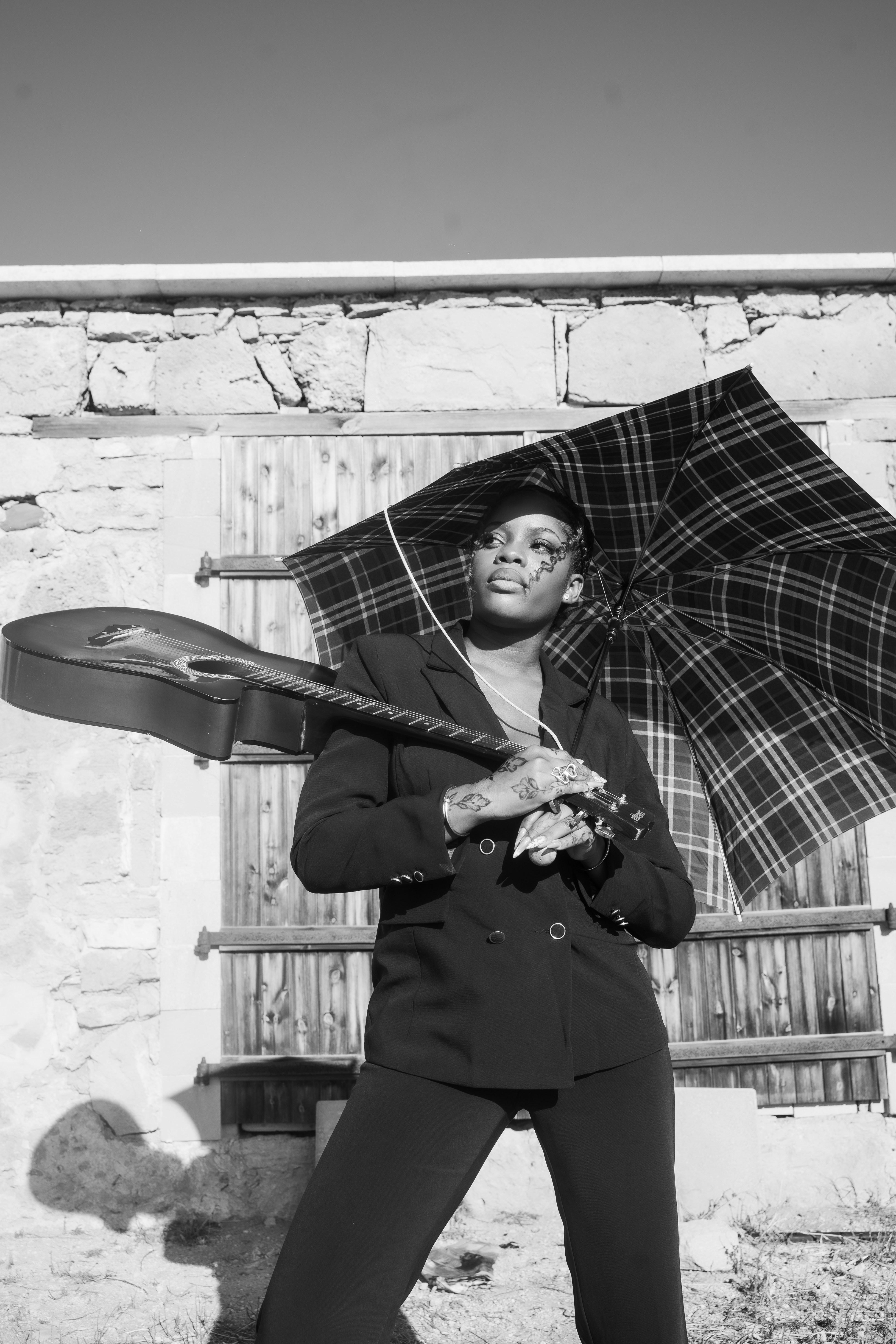 Woman holding guitar and umbrella against rustic wall