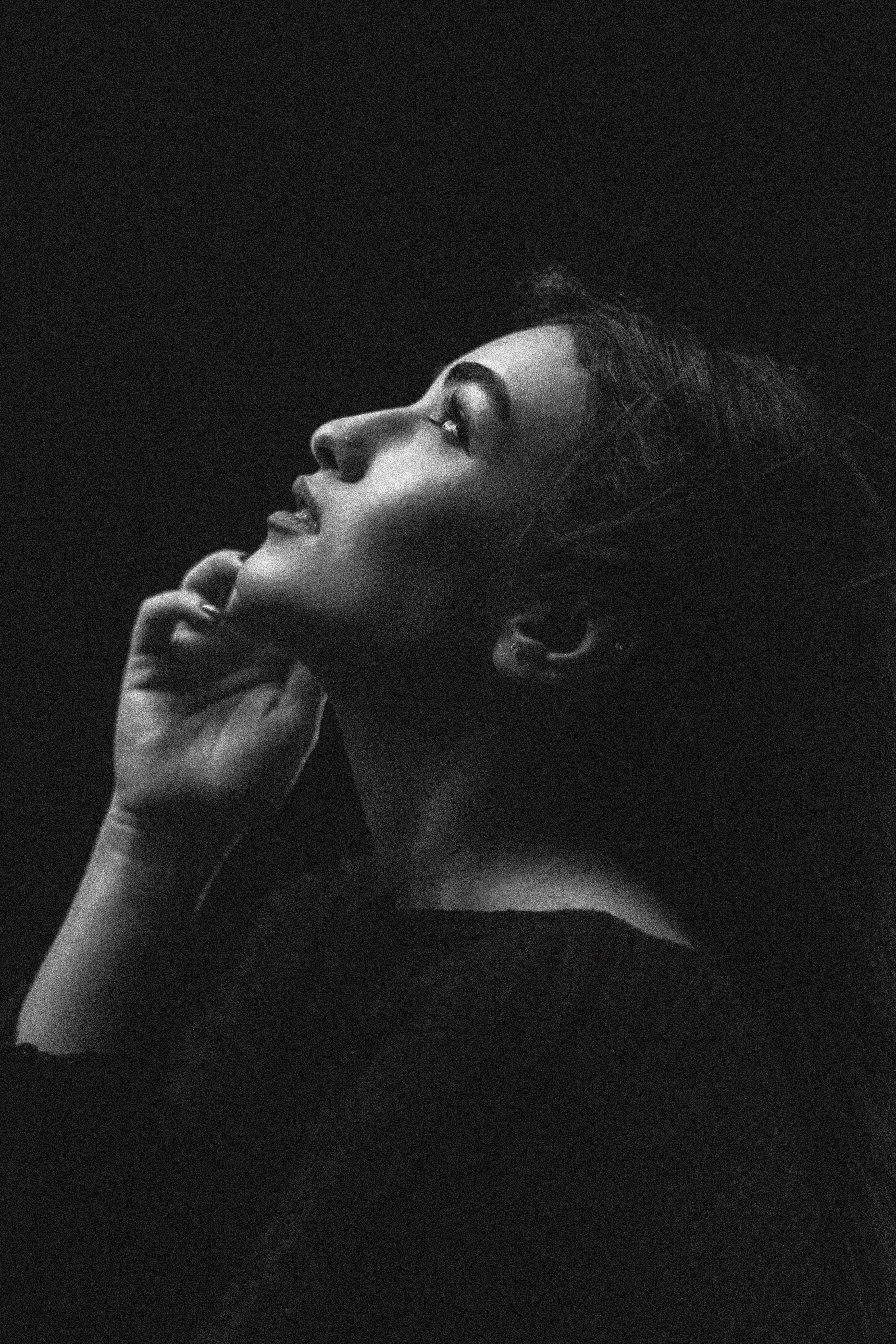 A young woman looks up thoughtfully against dark background.