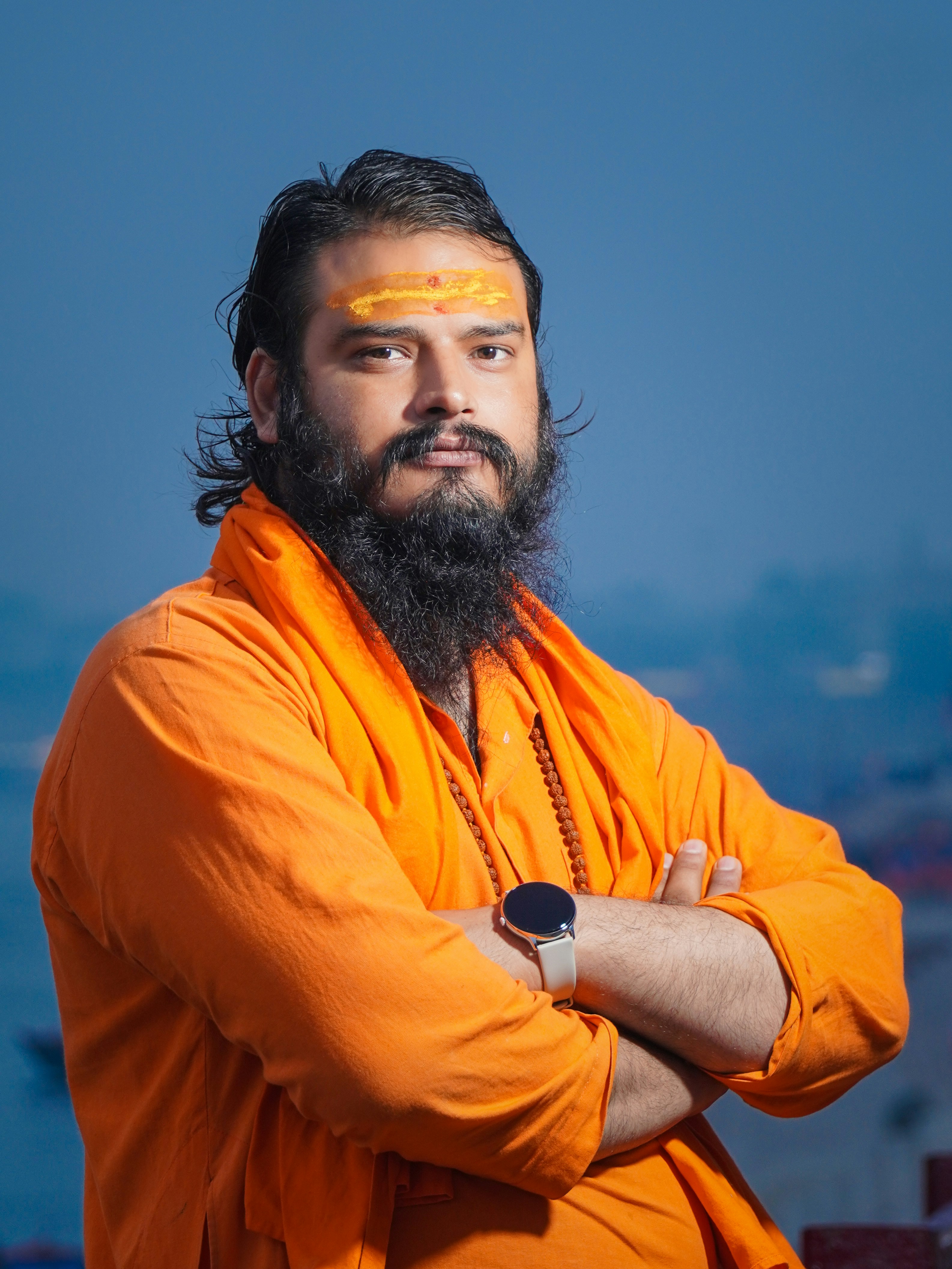 Man with beard wearing orange robes and forehead mark.