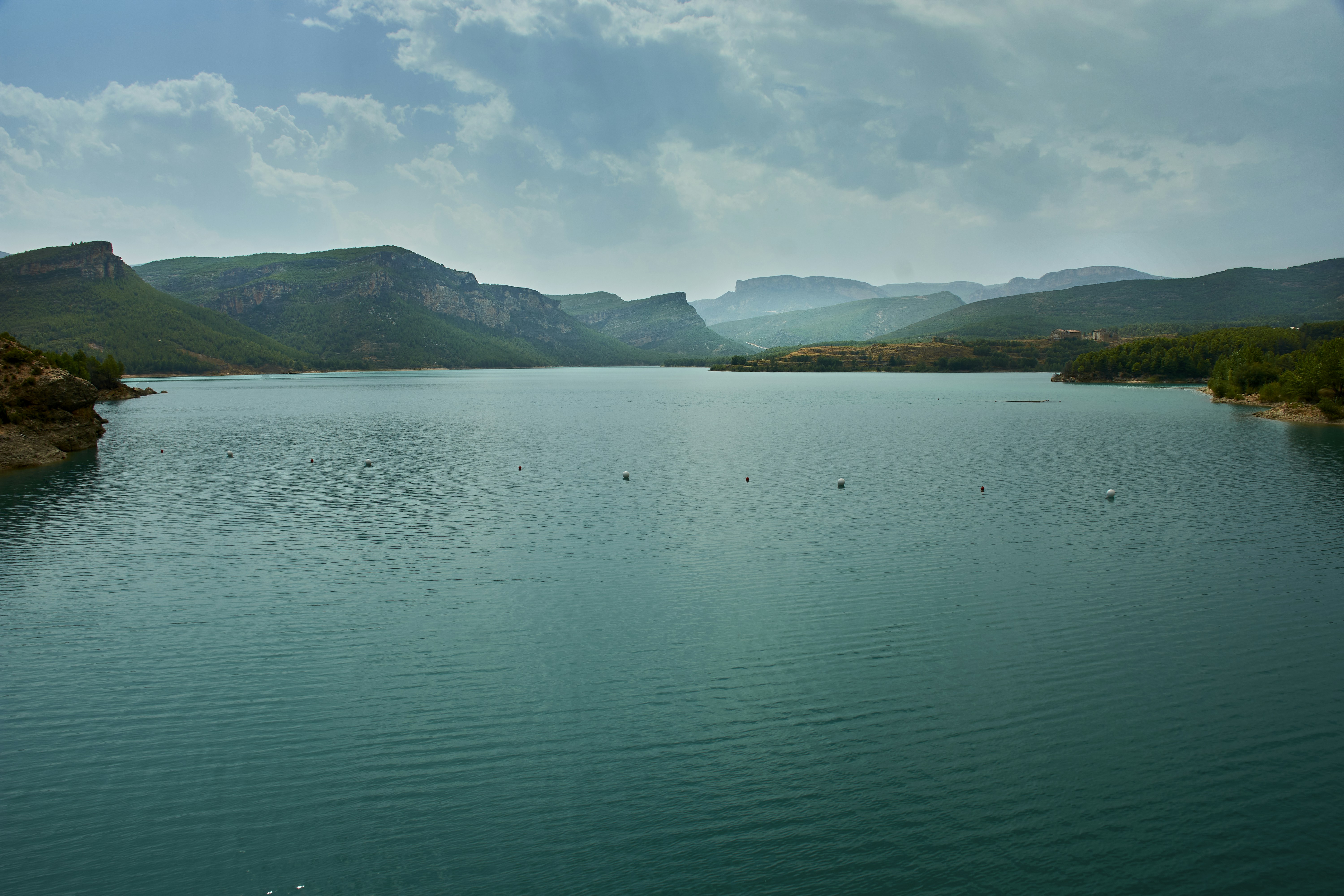 Vast blue lake surrounded by rolling hills under sky.