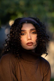 Young woman with curly hair wearing a brown turtleneck.