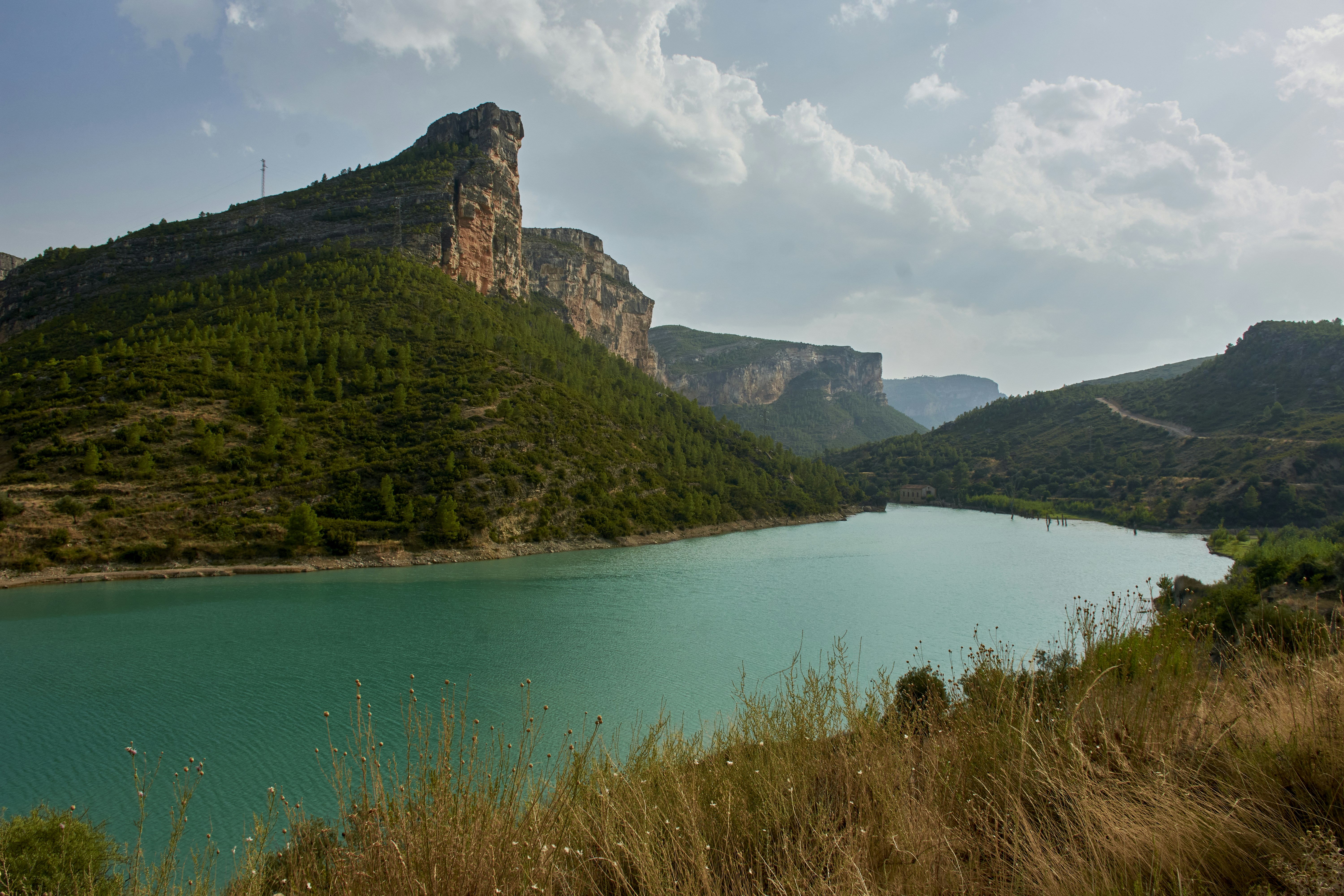 Turquoise lake surrounded by forested mountains under cloudy sky.