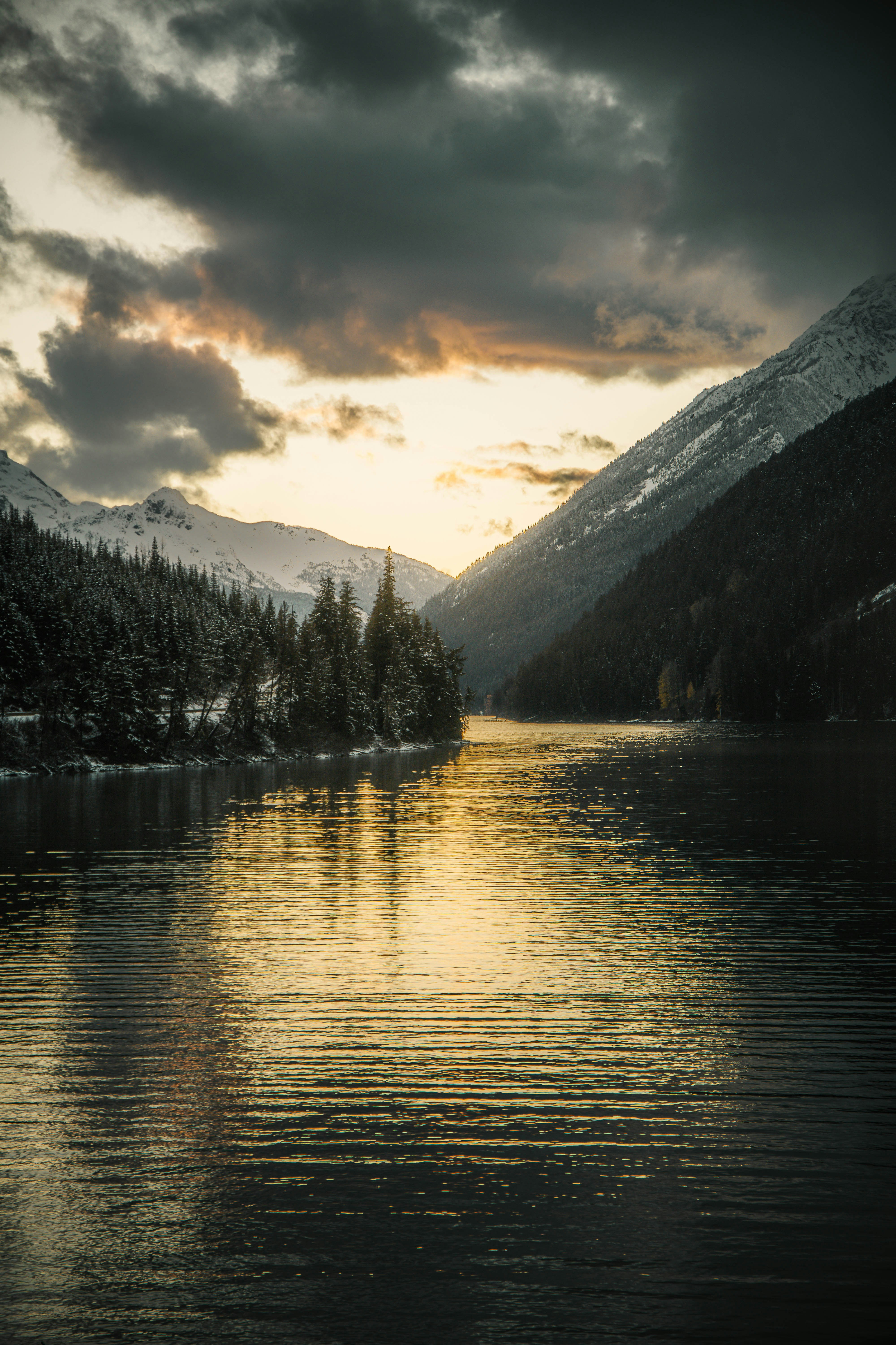 Snow-covered mountains reflect in a calm lake at sunset.