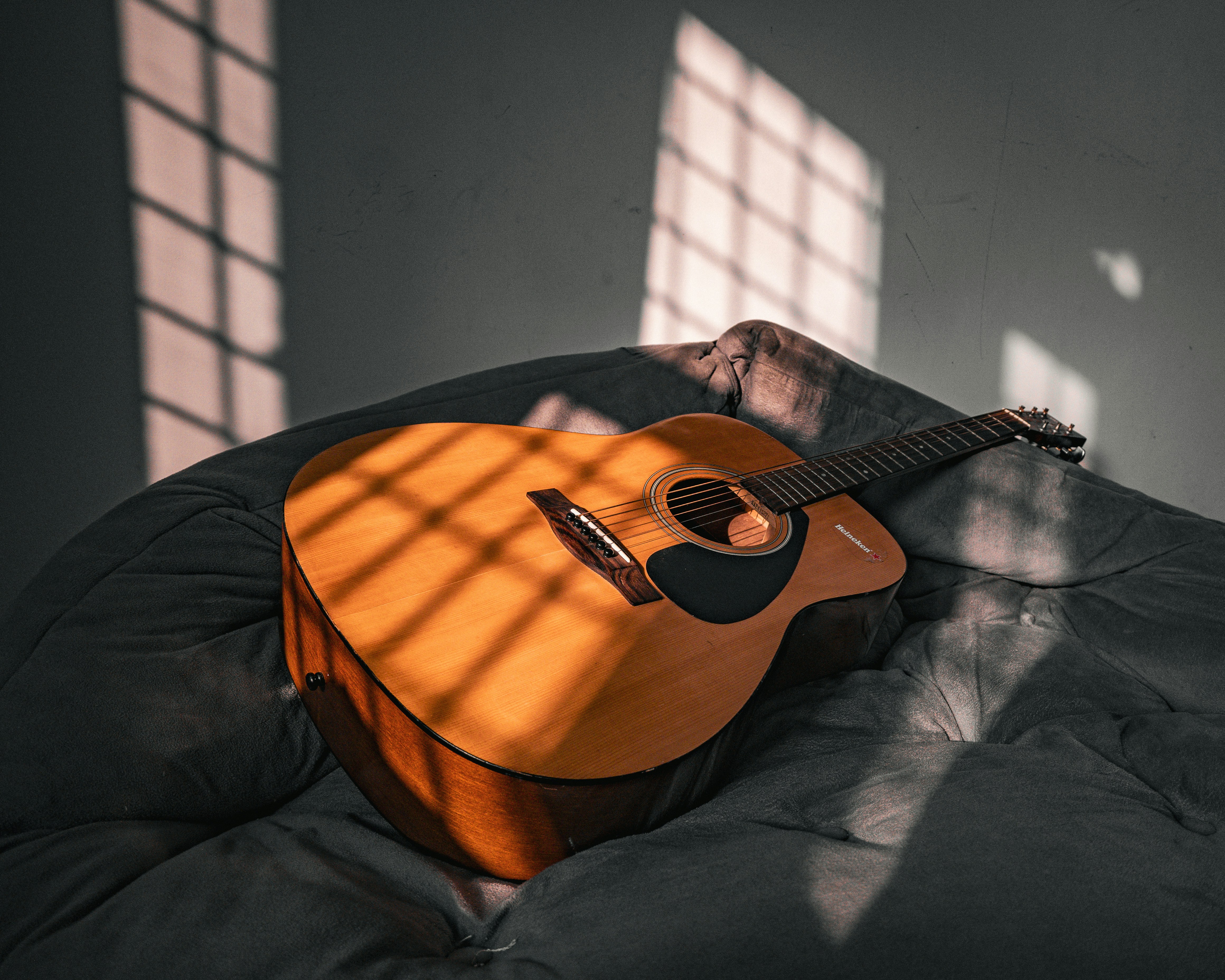 Acoustic guitar rests on a gray surface with sunlight patterns.
