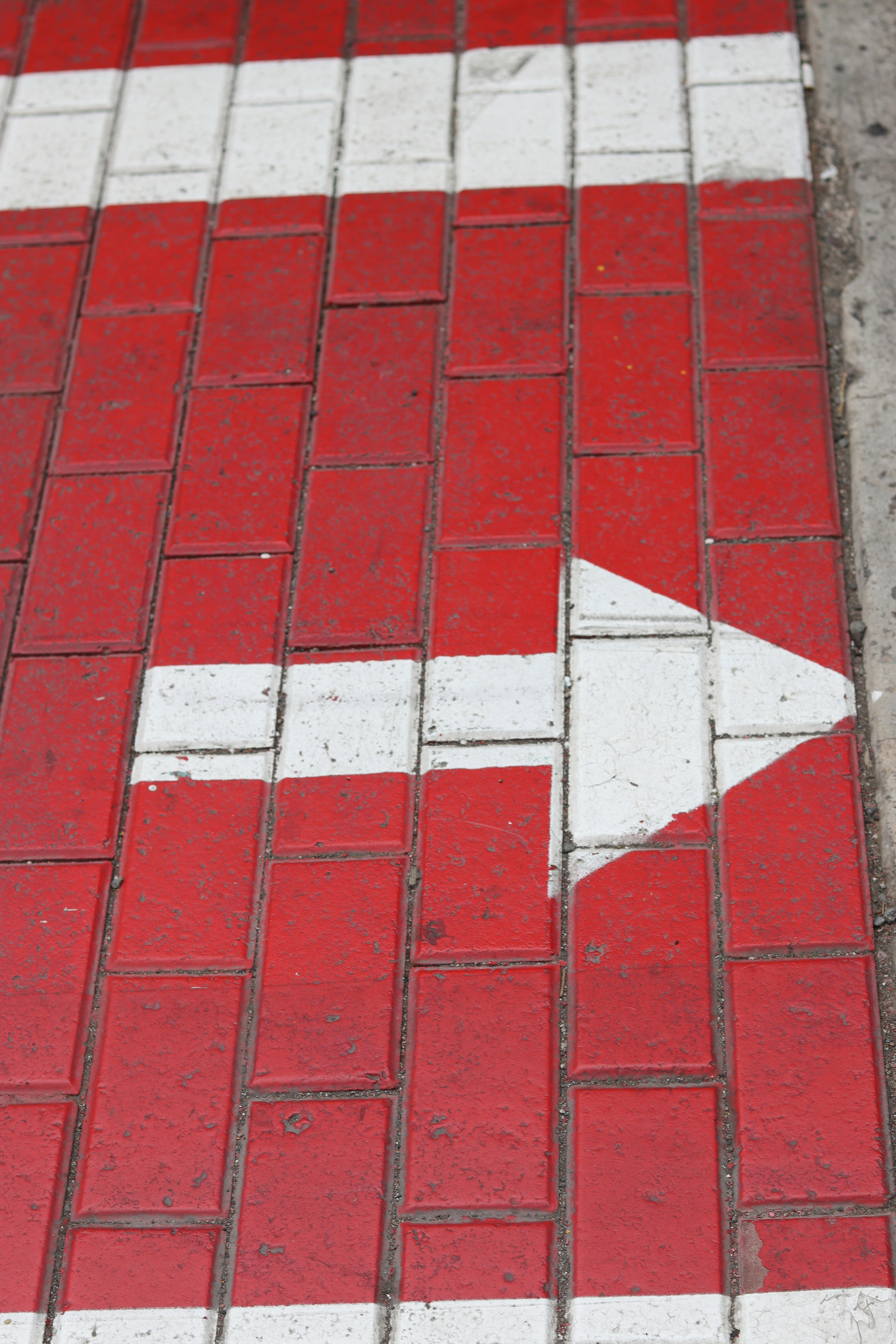 Red and white arrow painted on brick pavement.