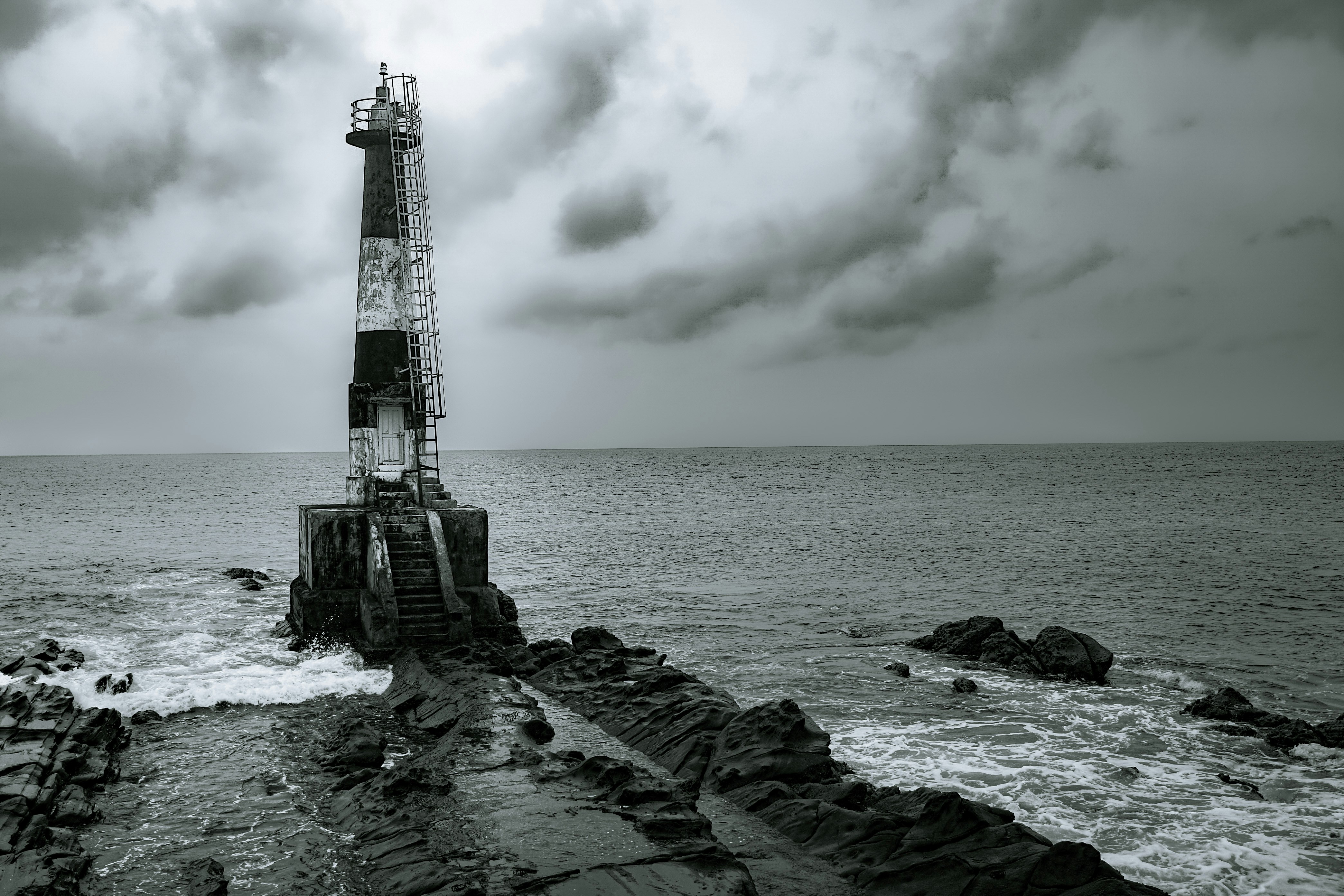 曇り空の下、岩だらけの海岸にある灯台