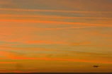 Airplane flying in the orange sky at sunset.