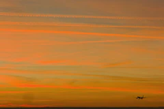 Airplane flying in the orange sky at sunset.