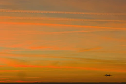 Airplane flying in the orange sky at sunset.