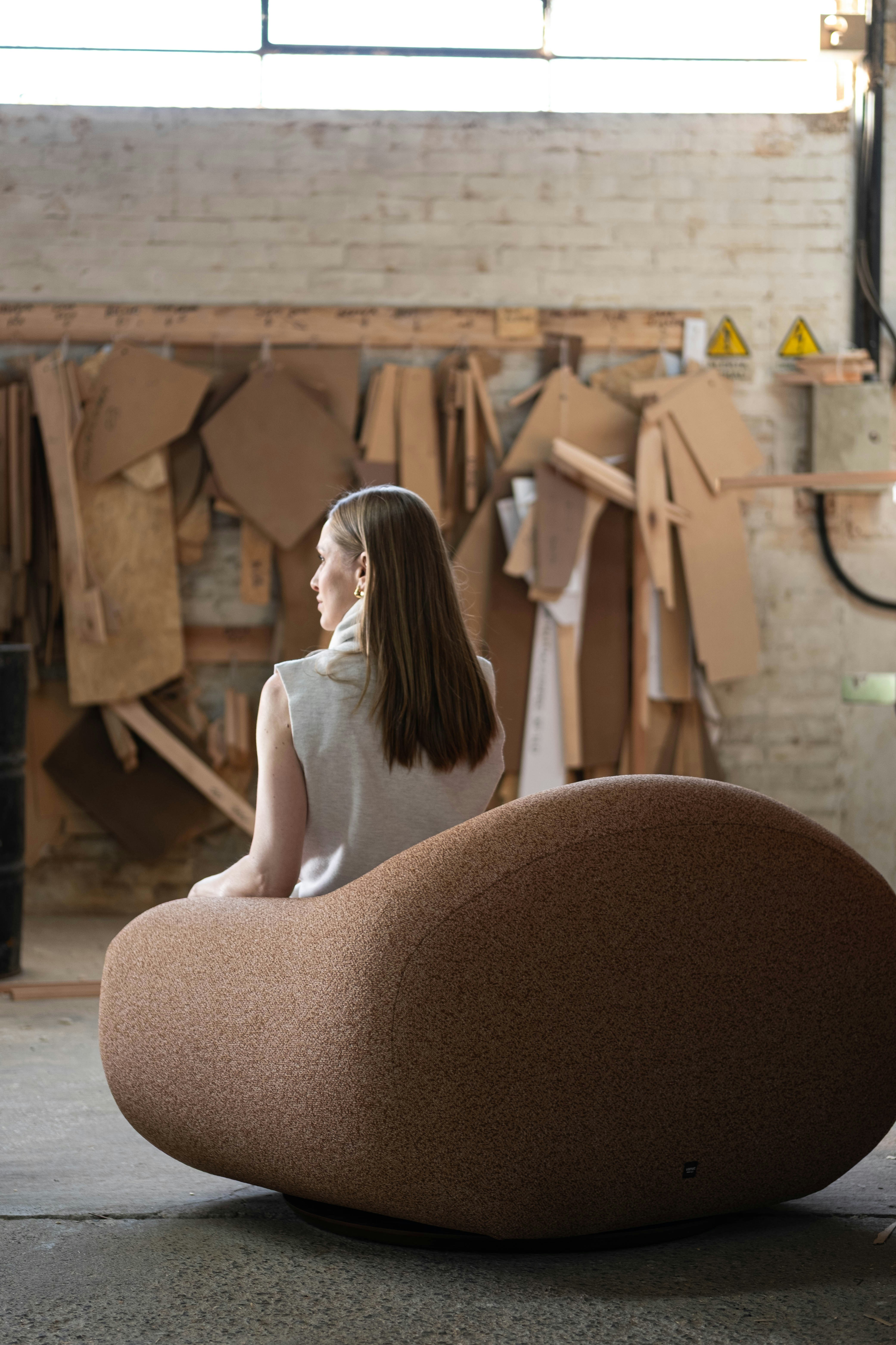 Woman sitting on a large, unique chair in workshop.