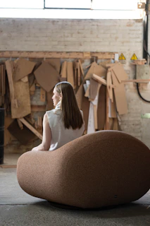 Woman sitting on a large, unique chair in workshop.