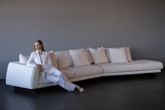 Woman in white suit sitting on a modern white sofa.