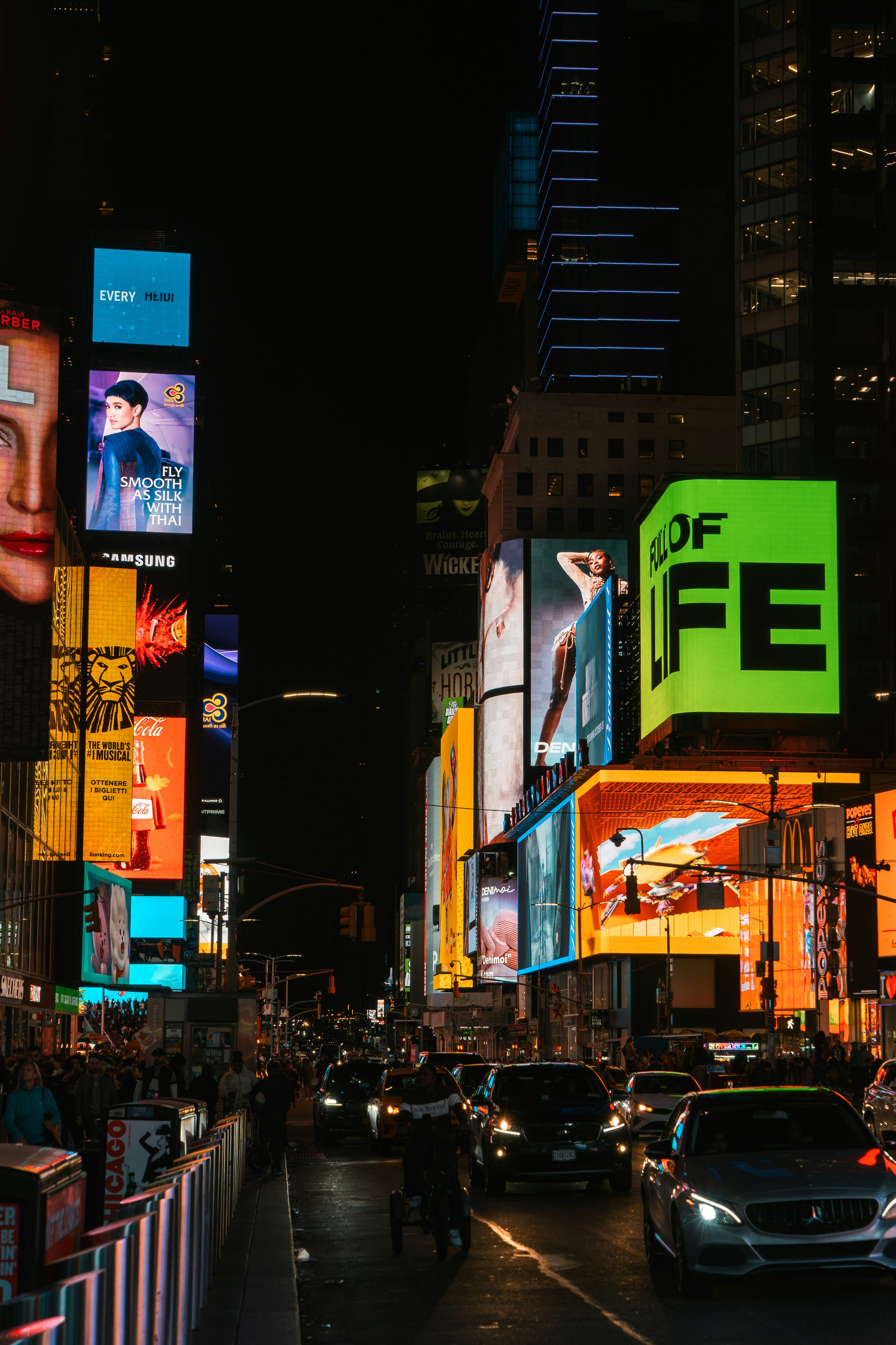 Brightly lit billboards illuminate a busy city street at night.