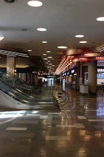 Modern shopping mall interior with escalators and shops.