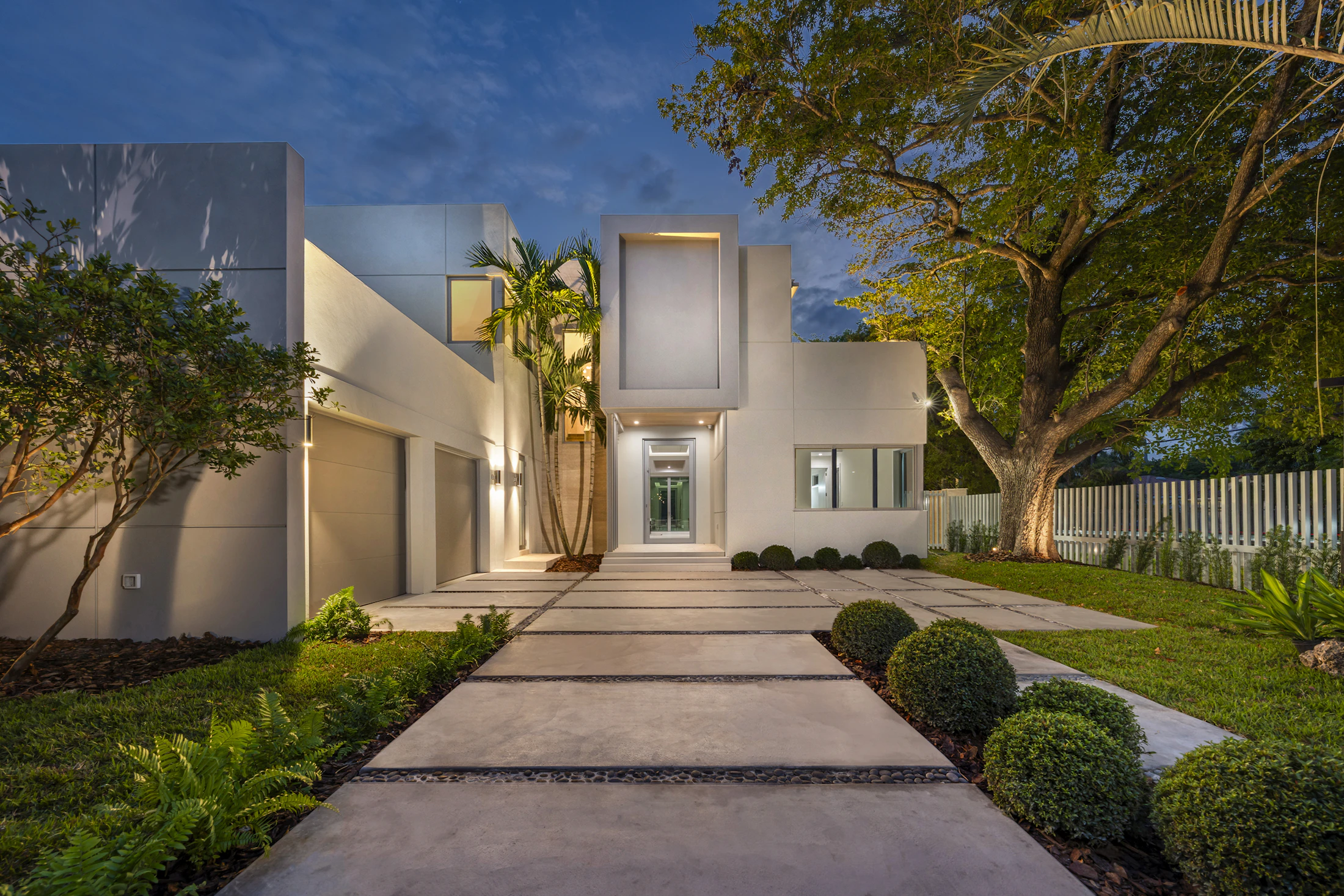 Modern white home with an illuminated pathway at dusk