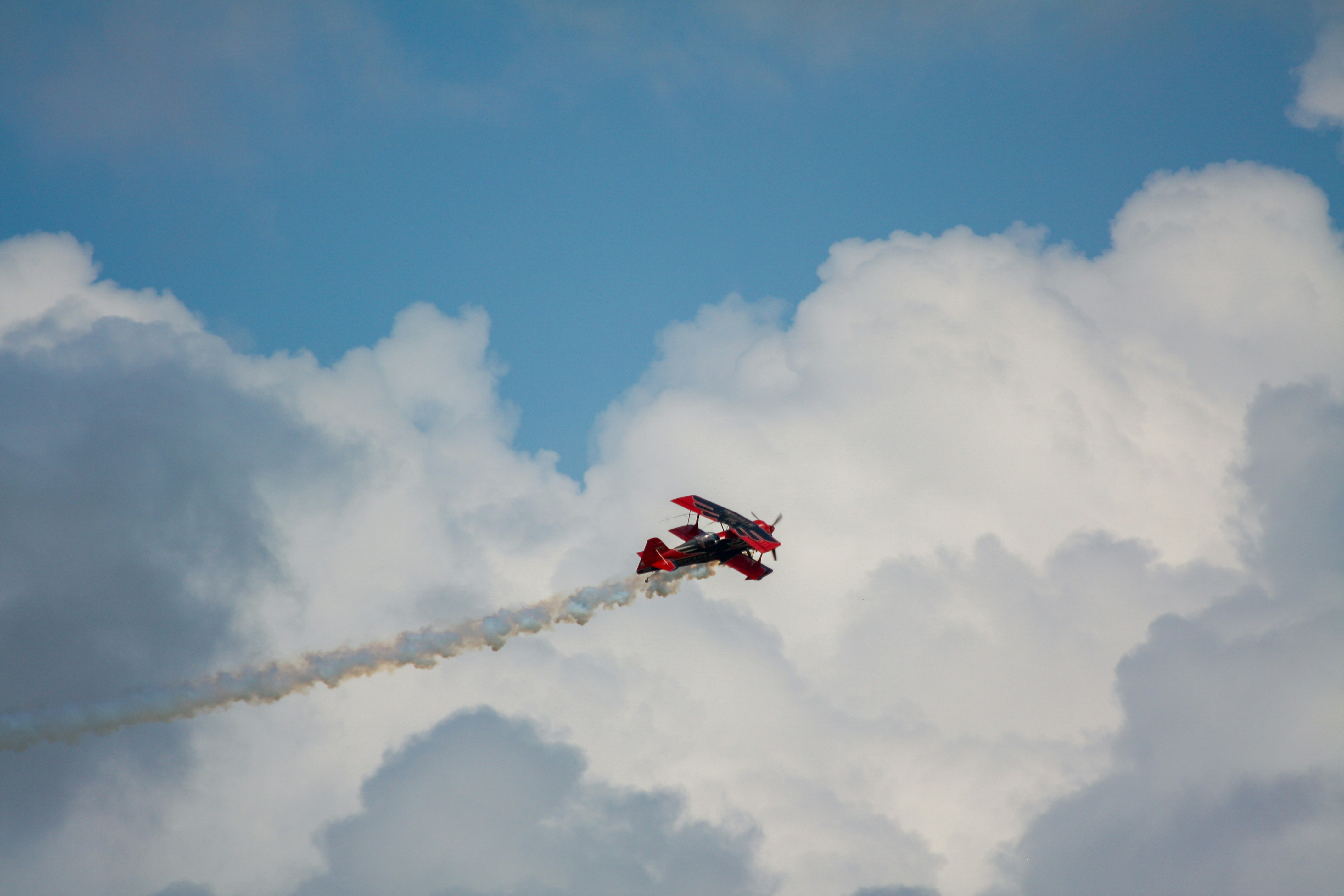 Red biplane flying through clouds leaving smoke trail