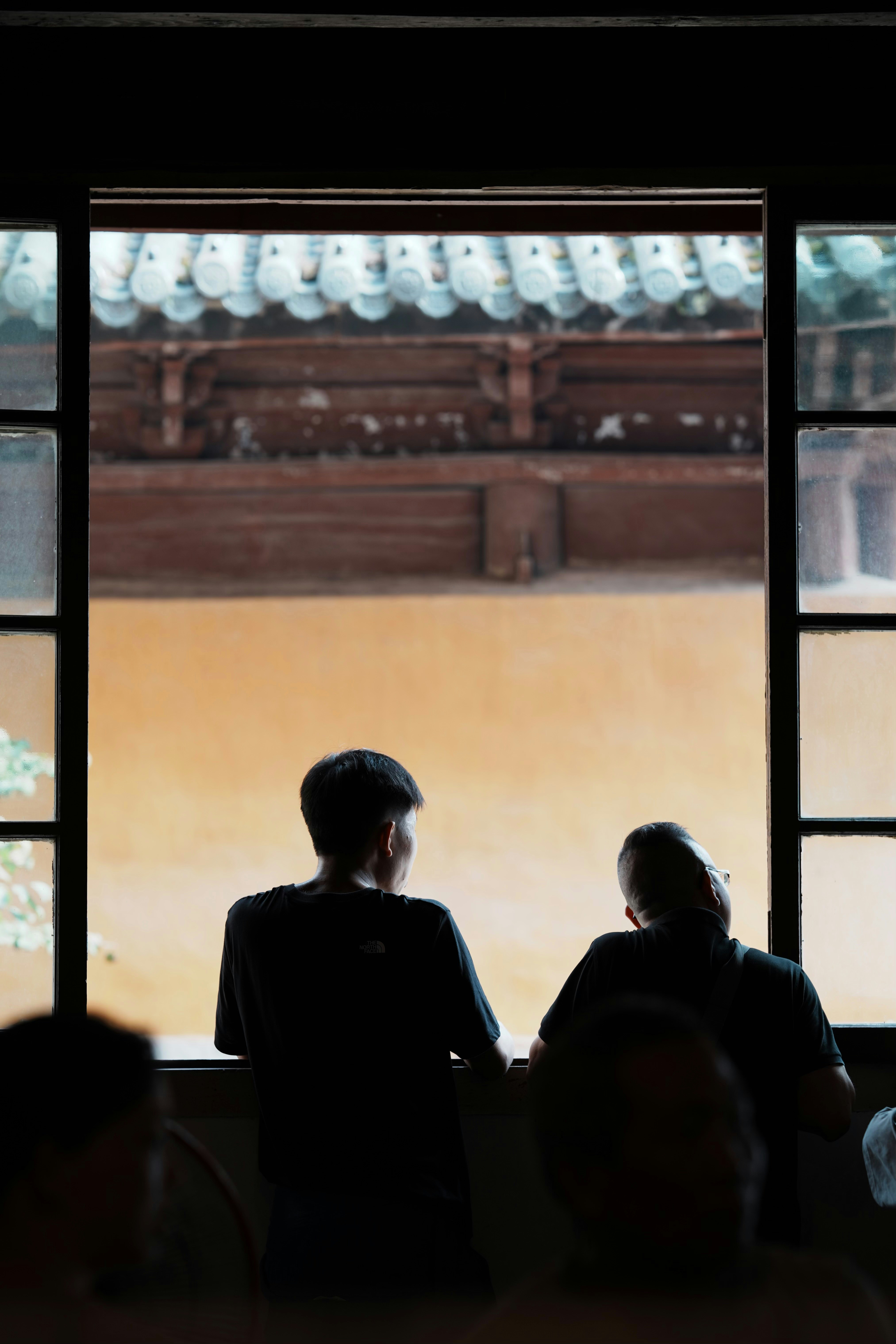 Two people look out a window at a building.