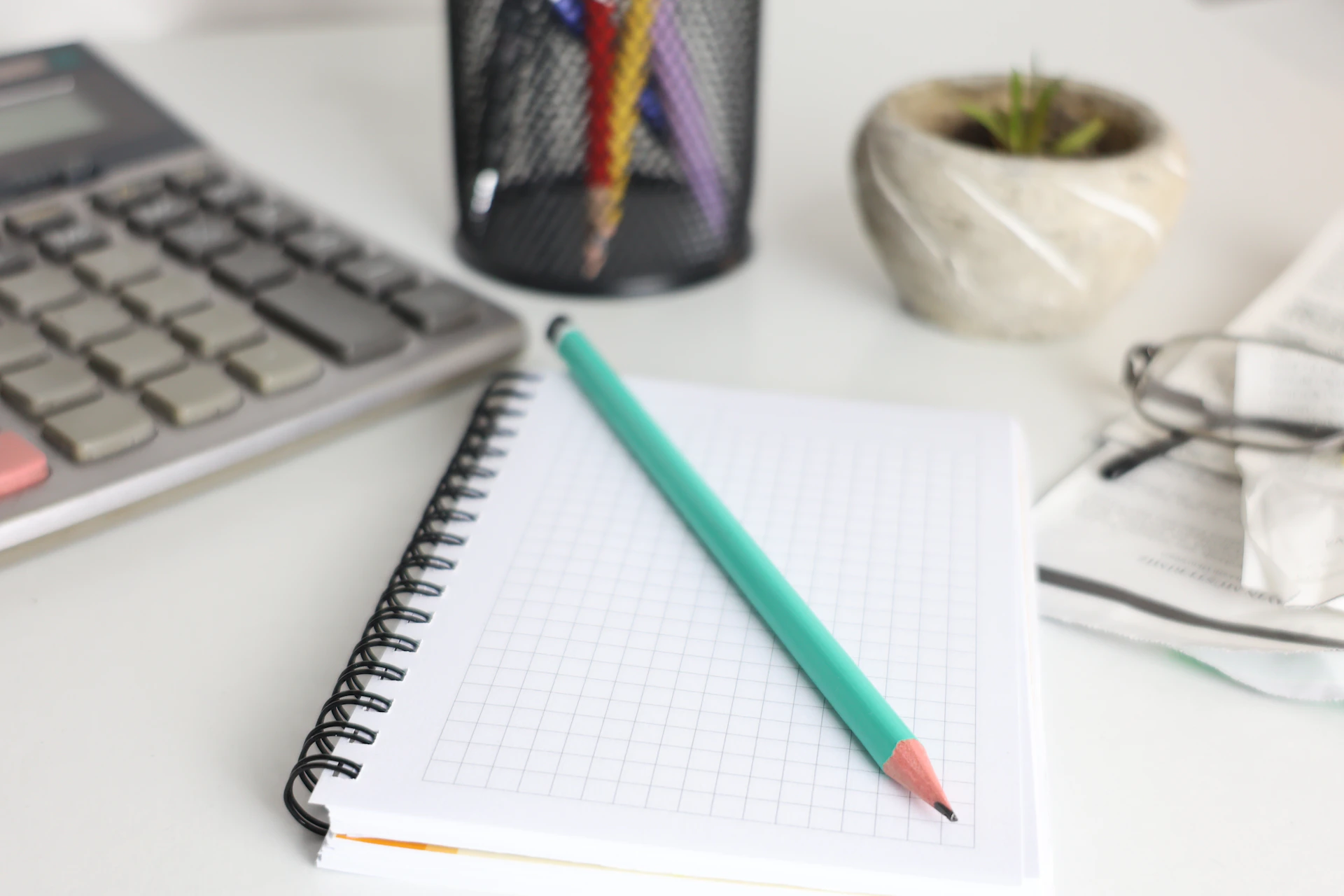 Desk with calculator, notebook, pencil, and plant.