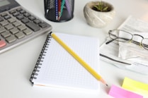Desk with calculator, notebook, pencil, and glasses.