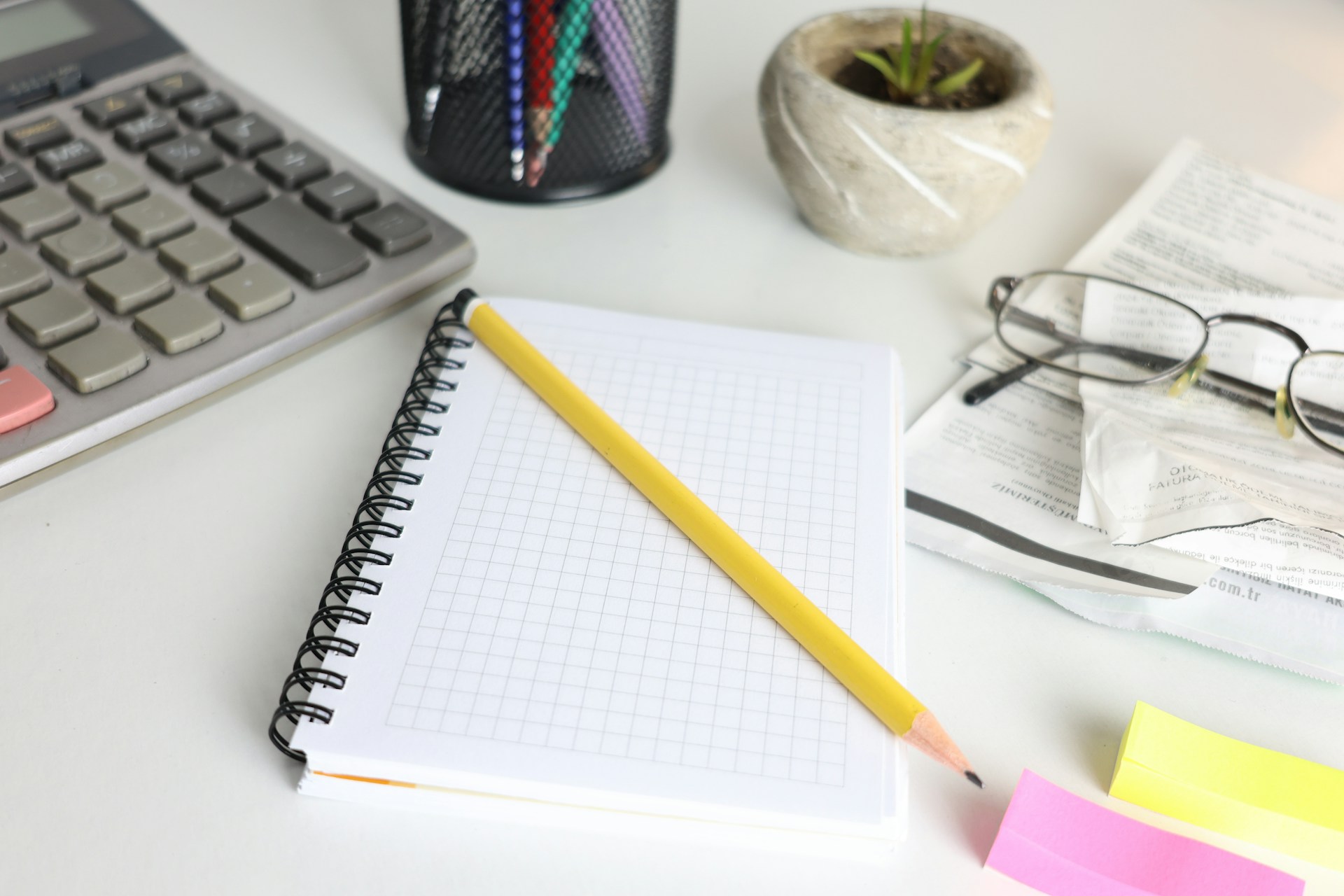 Desk with calculator, notebook, pencil, and glasses.