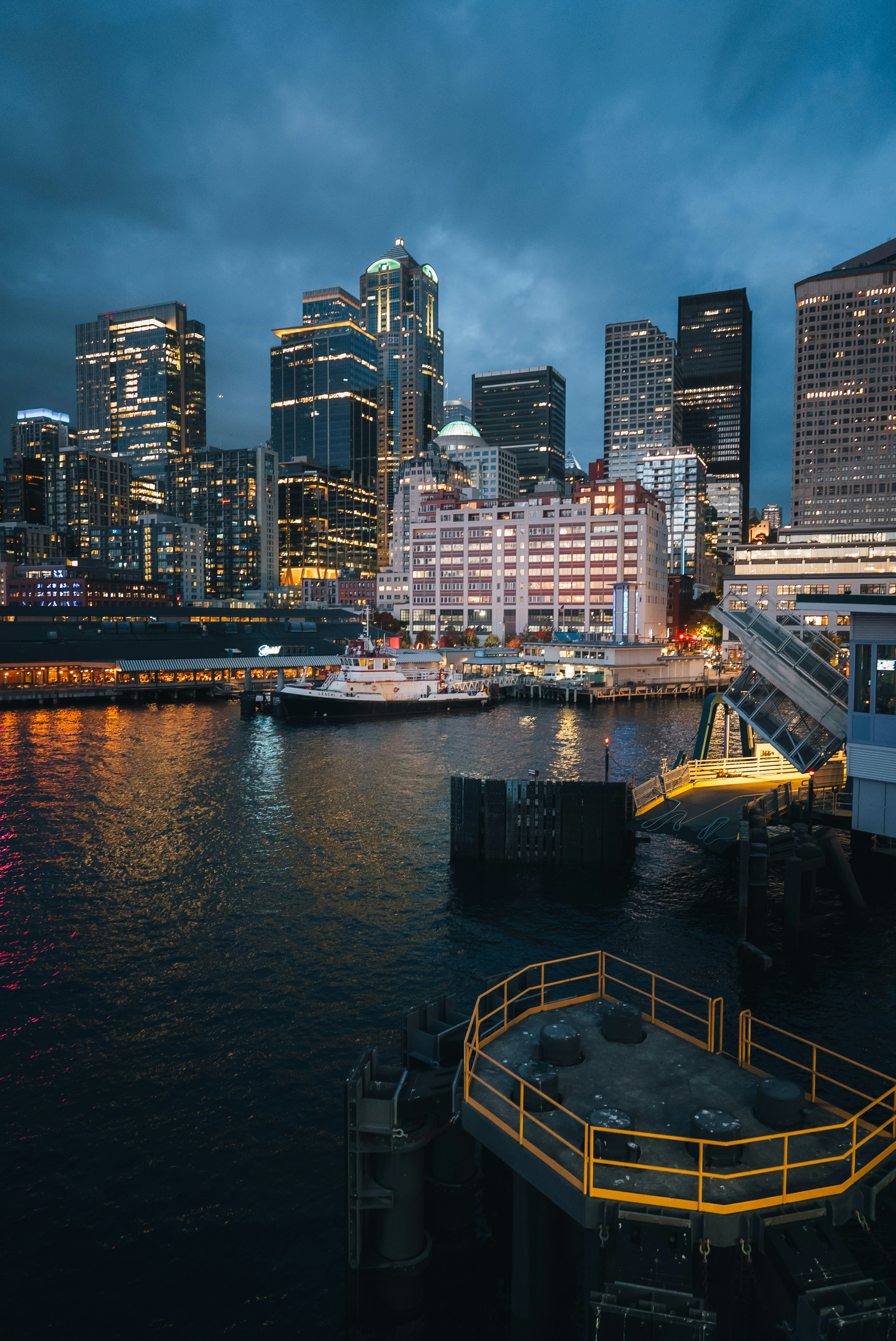City skyline with waterfront buildings and boats at dusk.