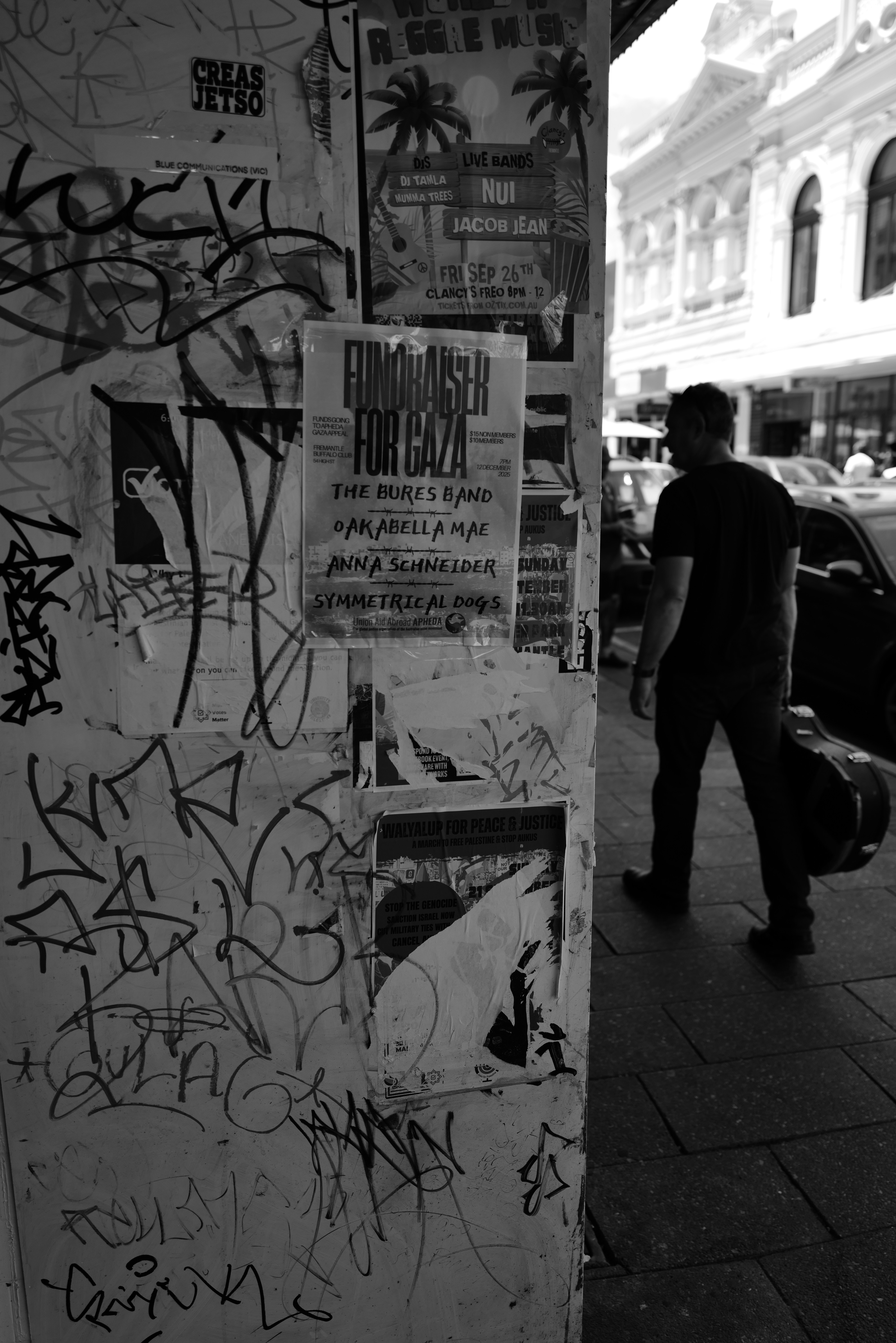 Man walks past graffiti-covered wall with posters.