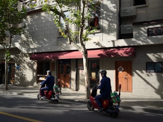 Two people riding electric scooters on a street.