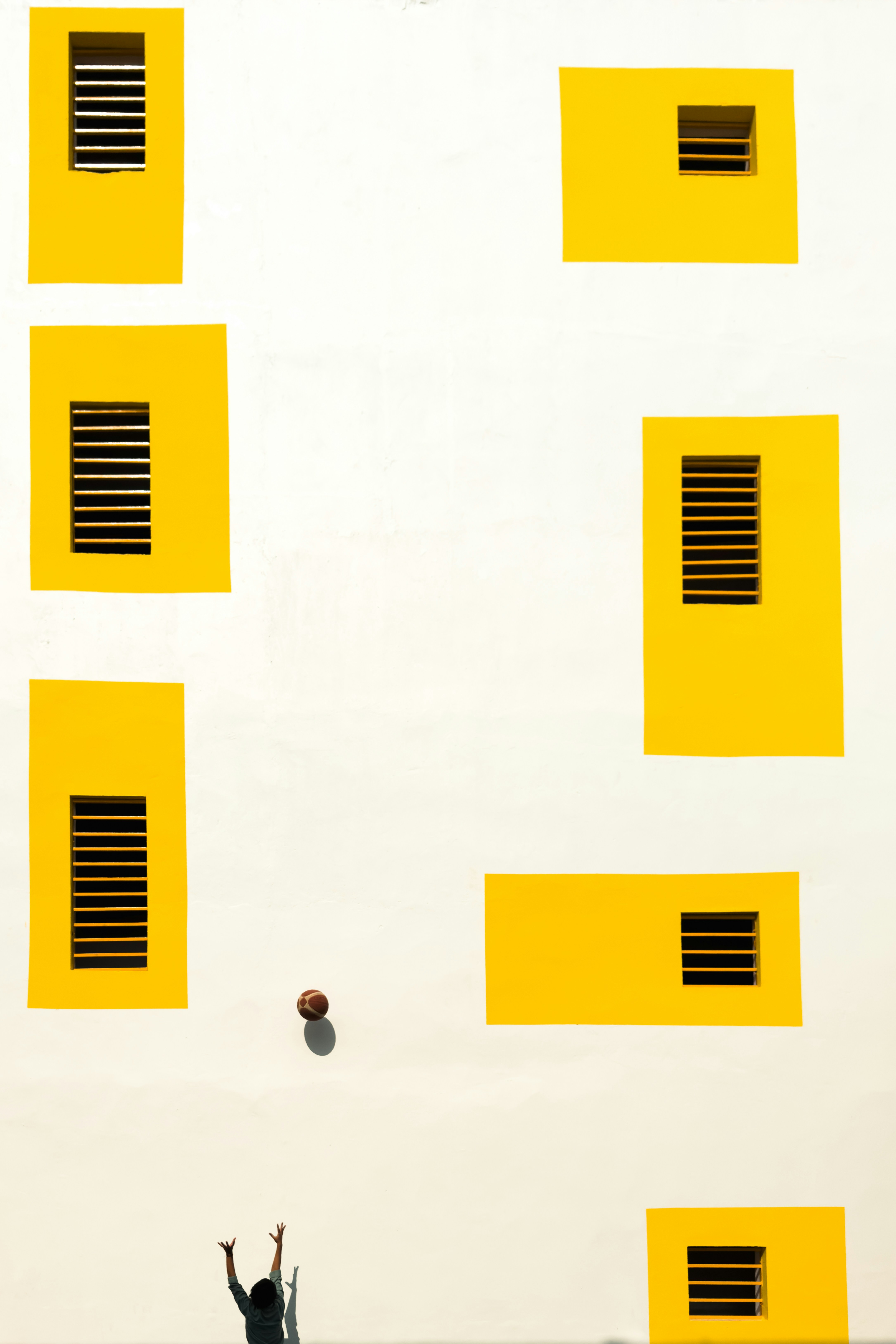 Person throwing ball against yellow windowed wall