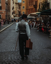 Man in vintage clothing walks down cobblestone street.