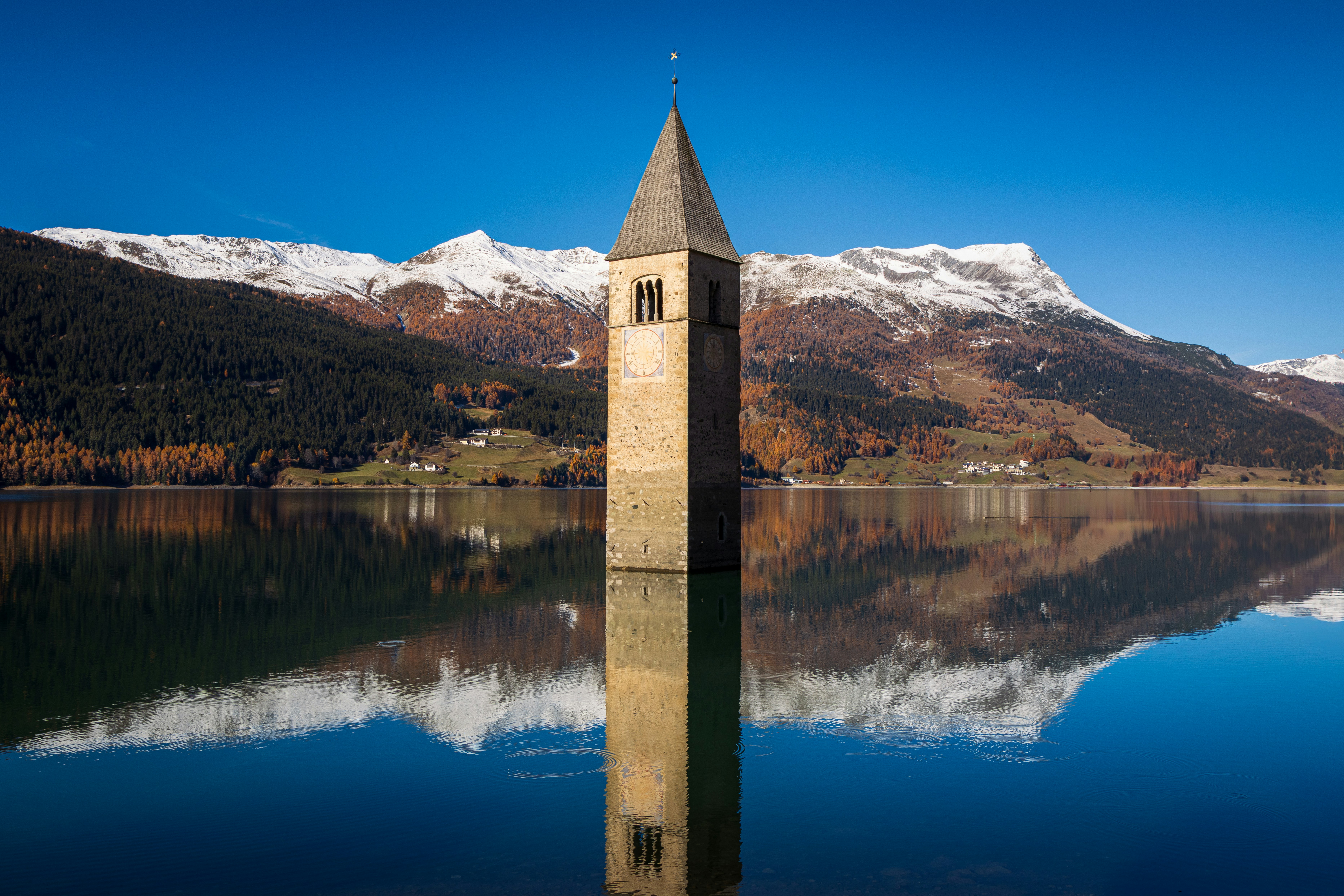 A submerged church tower reflects in calm water