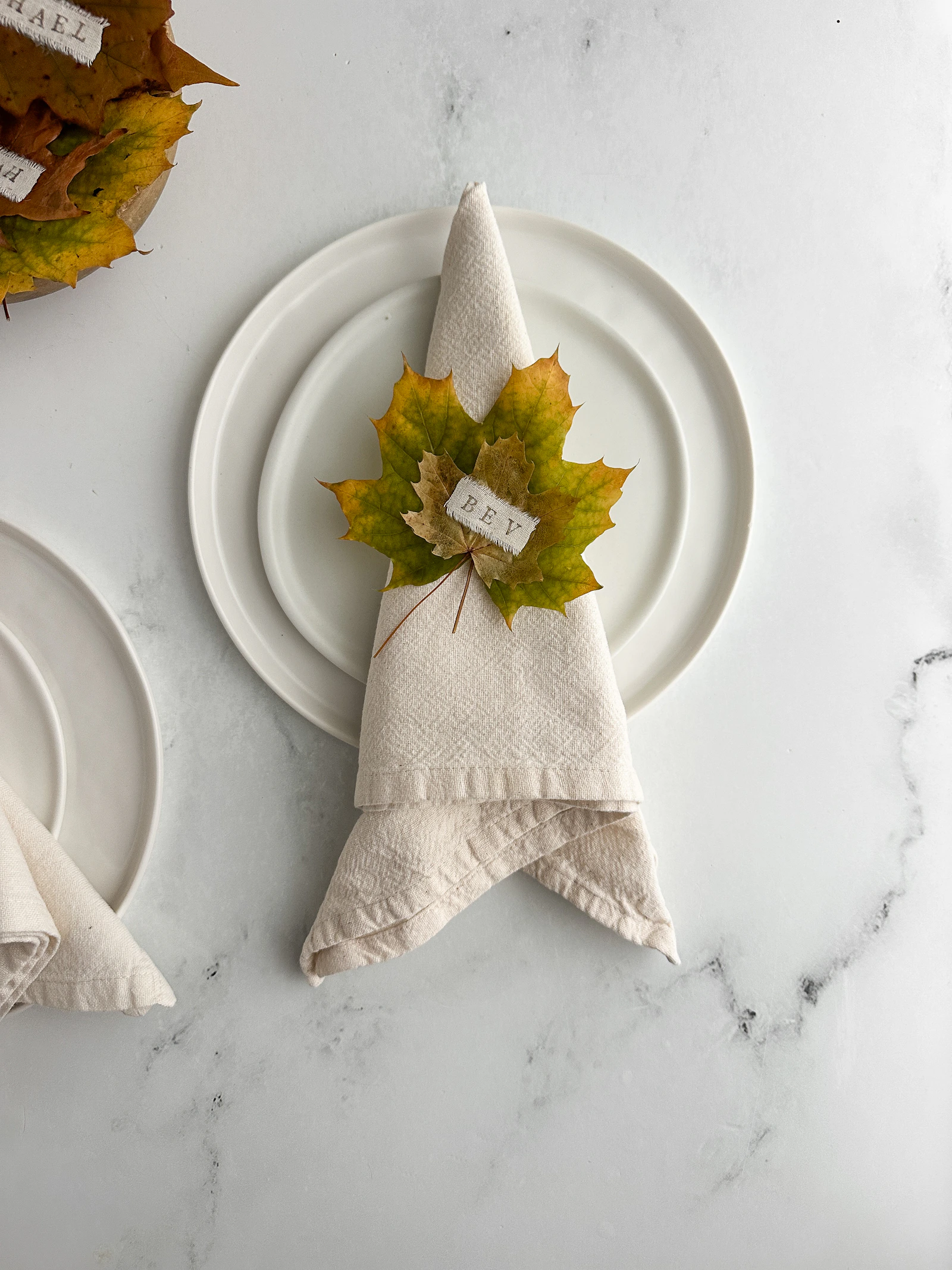 A linen napkin and autumn leaf place card on stacked white plates