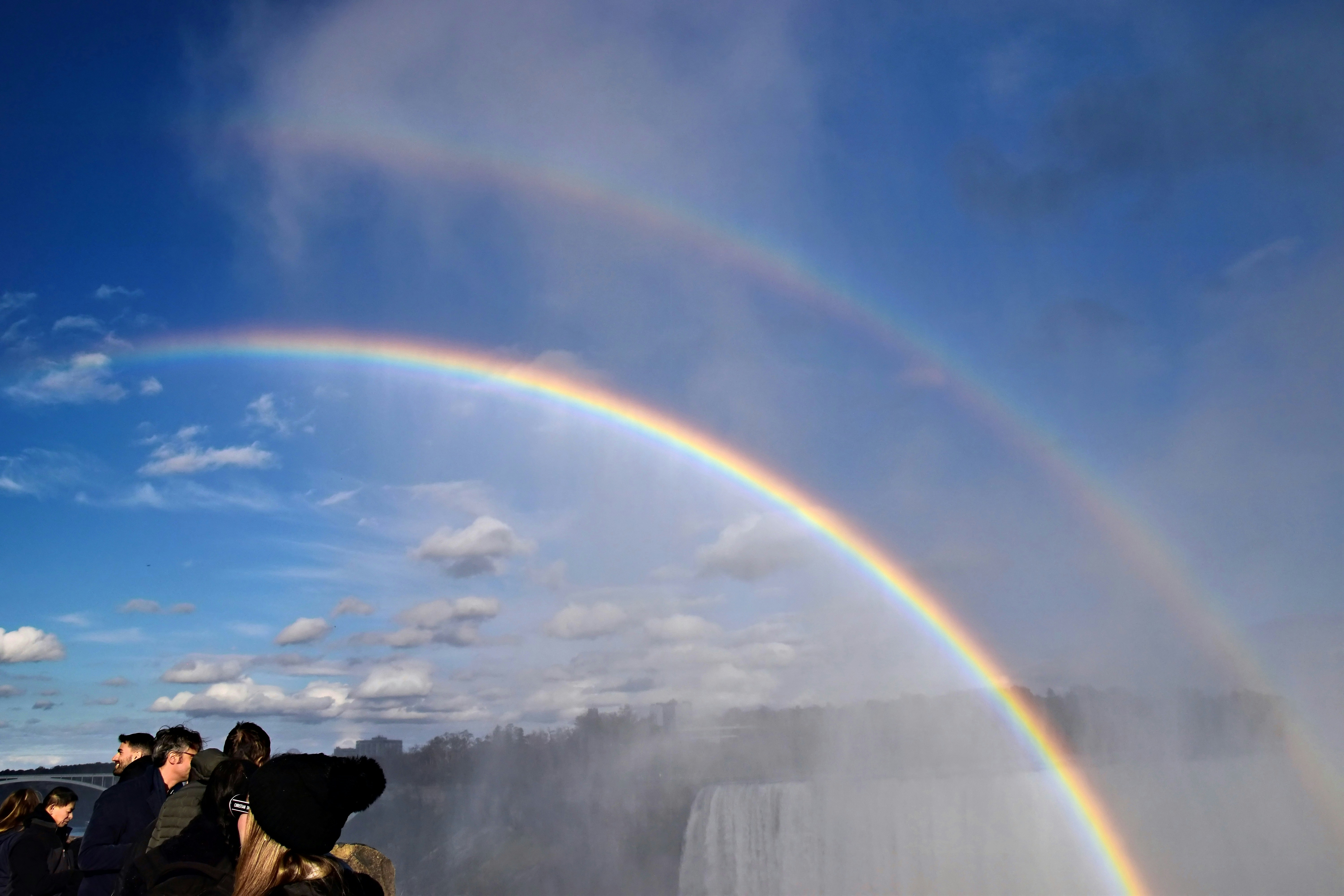 Double rainbow over misty waterfall with onlookers