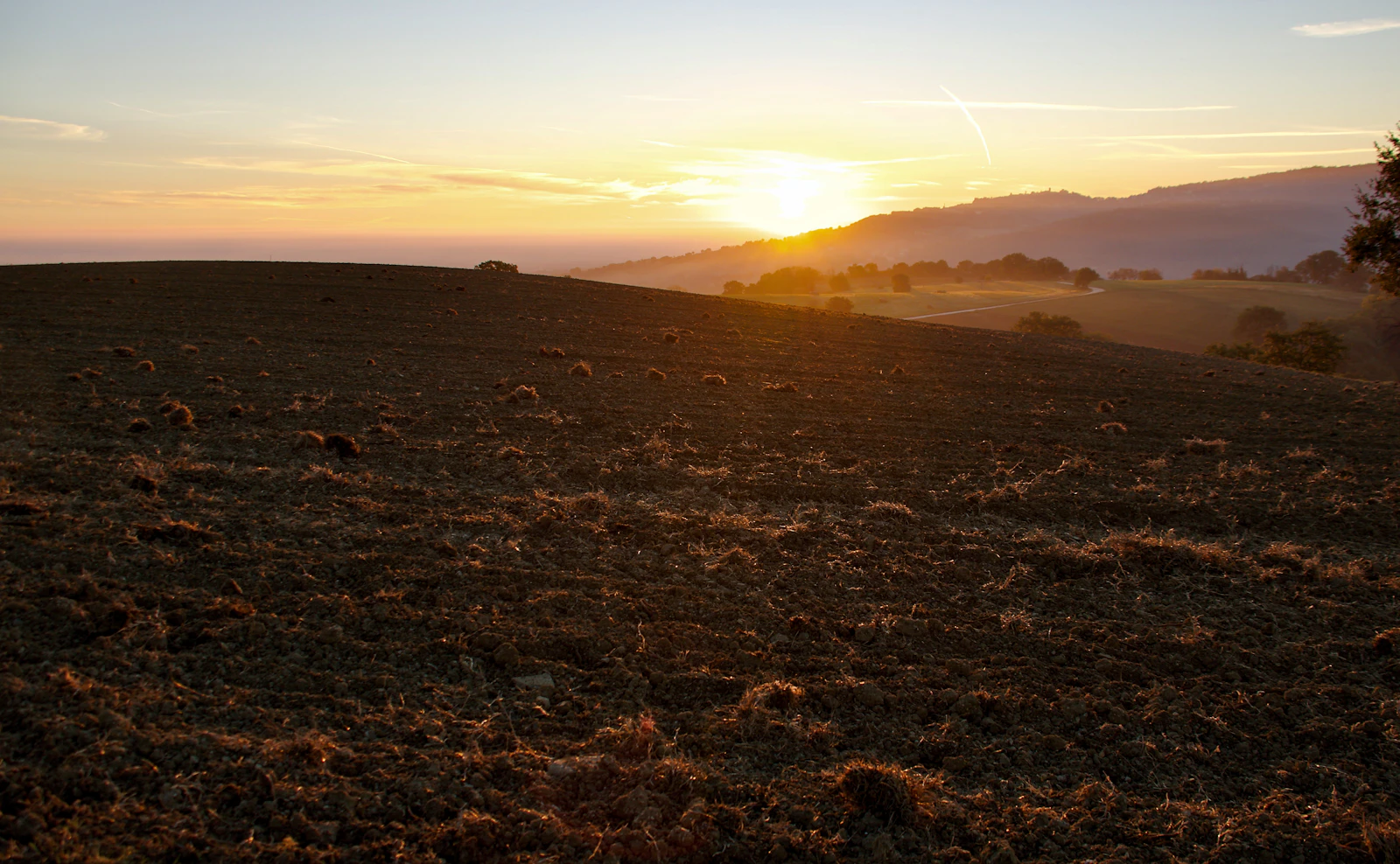 Sunrise breaking over misty agricultural fields and rolling hills at dawn