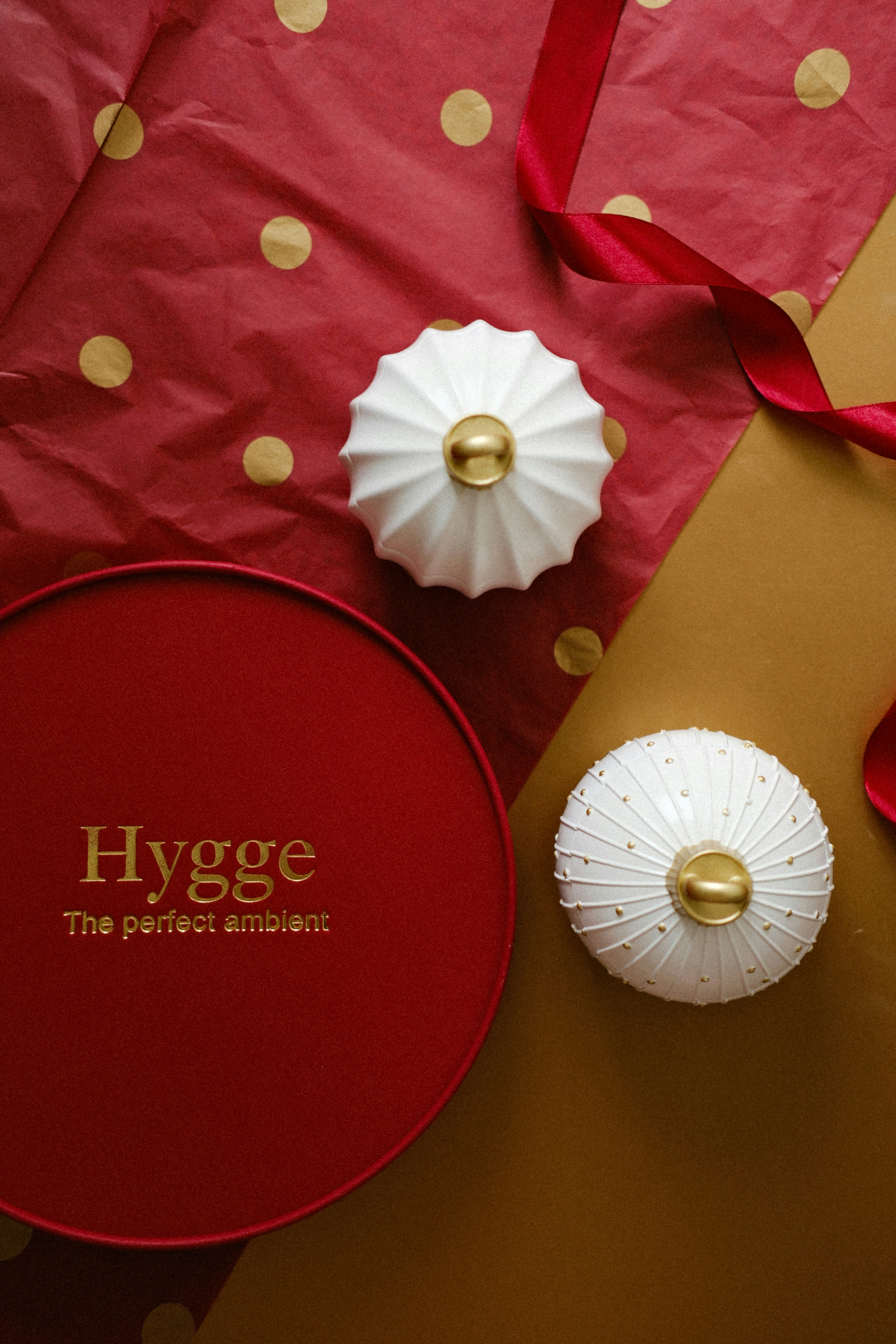 Two decorative white ornaments with gold accents on festive wrapping.