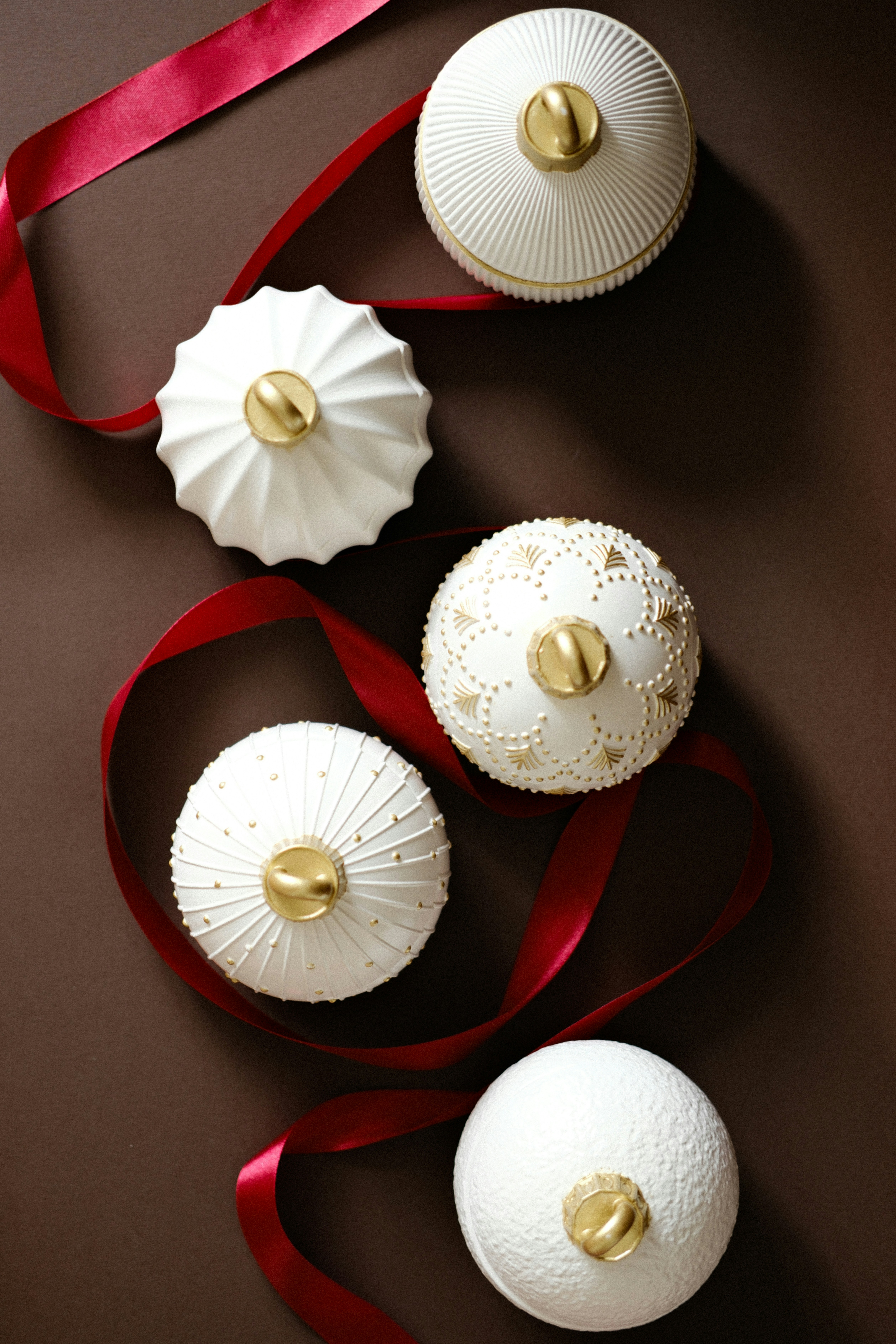 Four decorative white ornaments with gold accents and ribbon