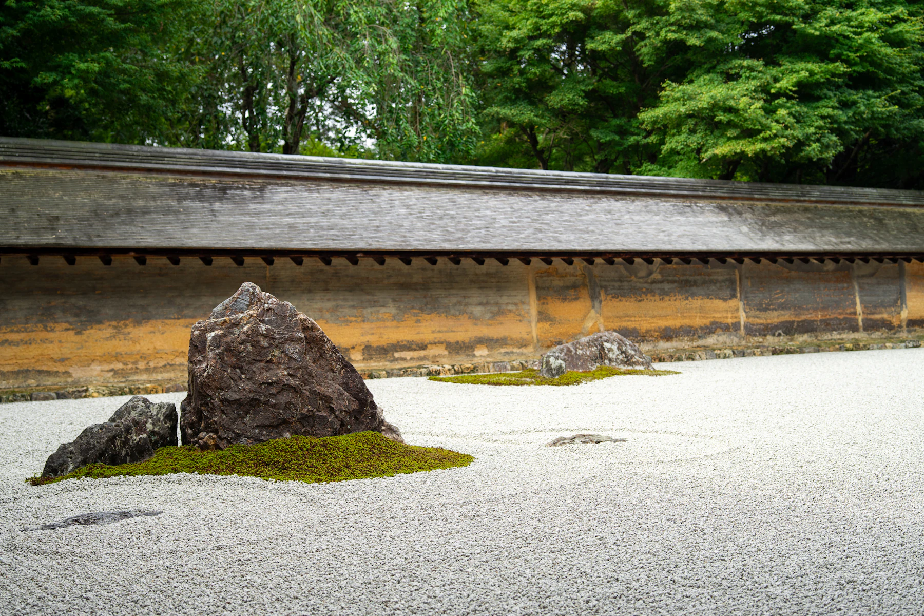 A large dark stone leading two smaller stones on a low moss island in a raked gravel garden