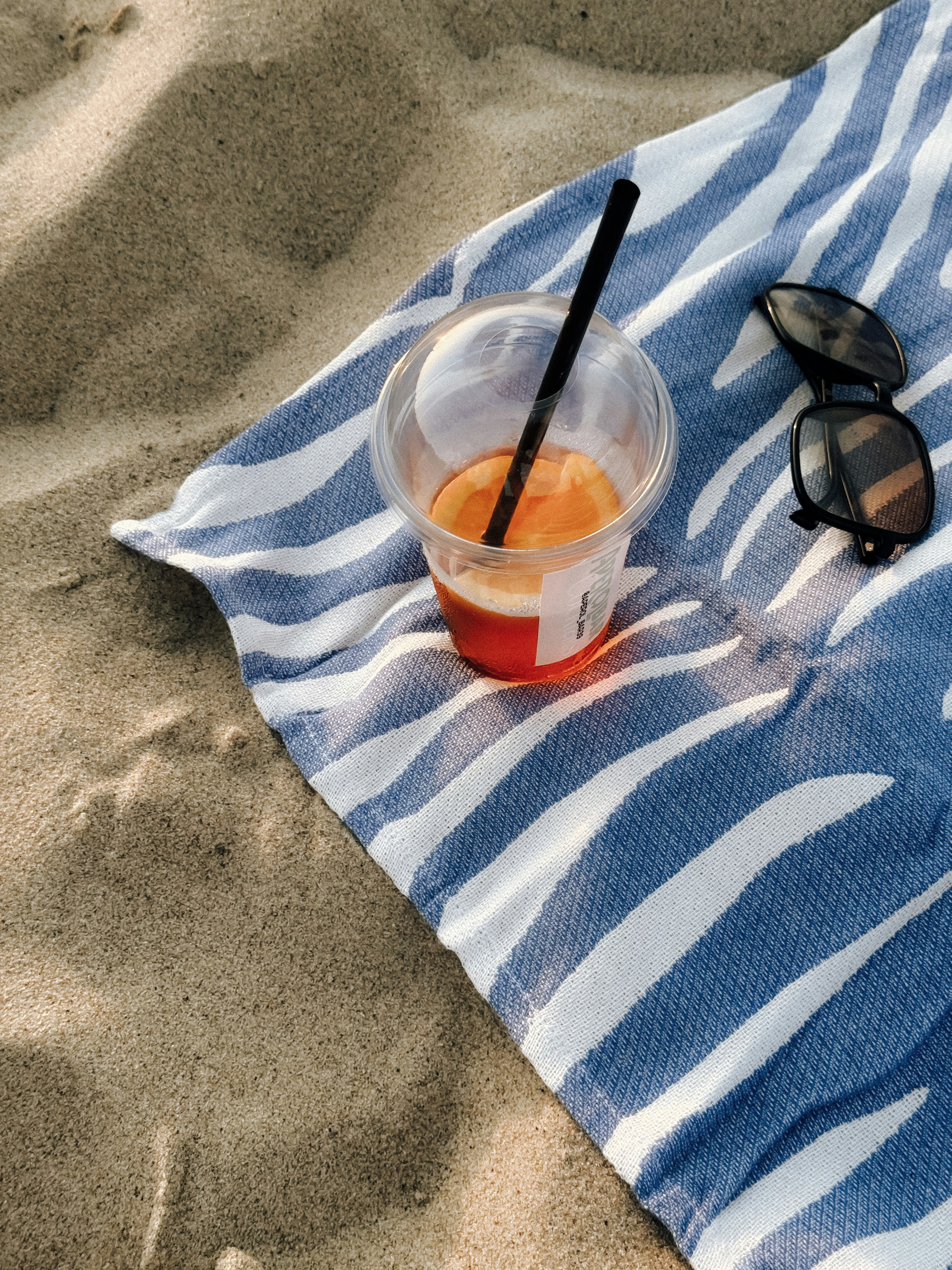 Drink and sunglasses on a beach towel.
