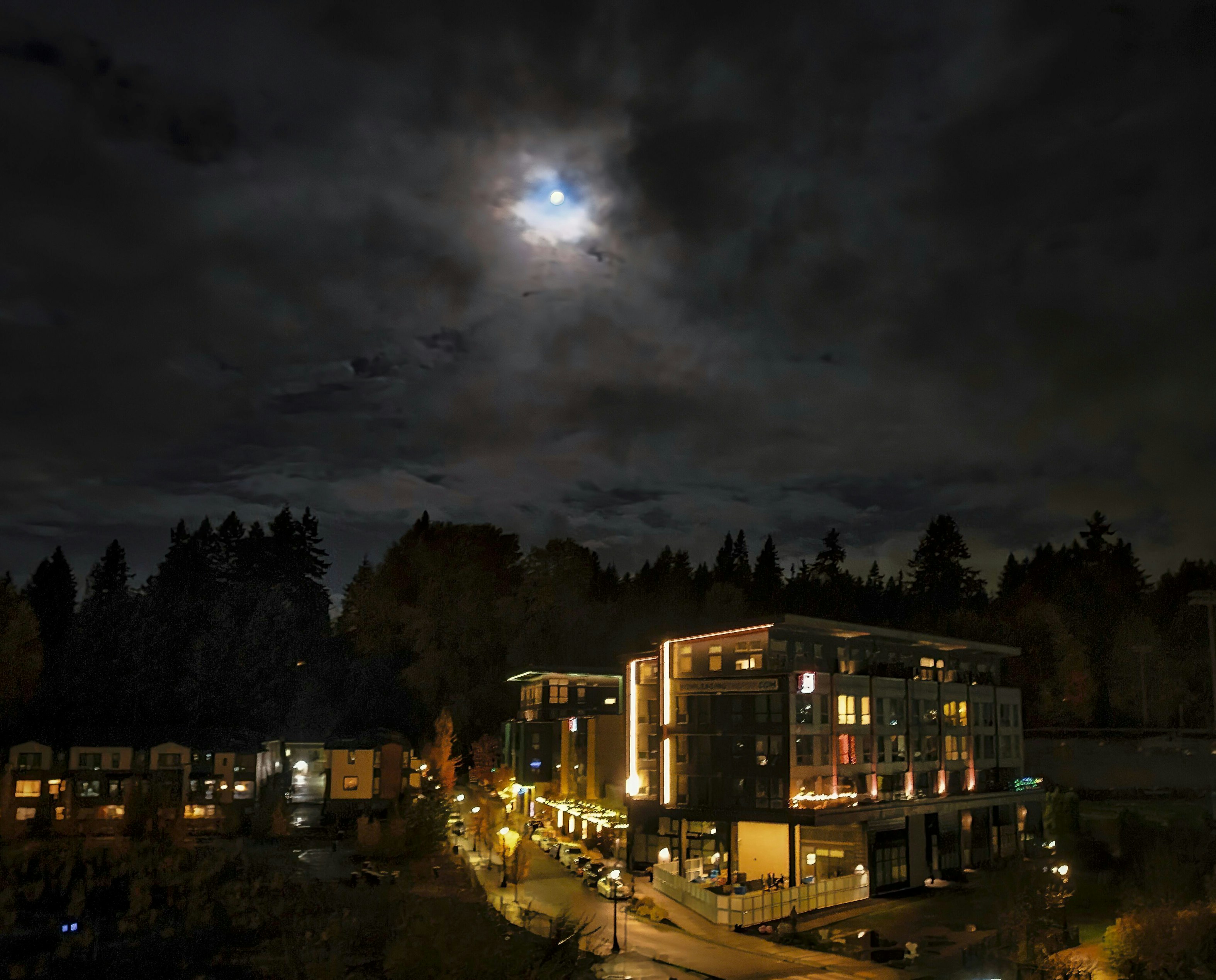 Buildings illuminated at night under a cloudy moonlit sky.
