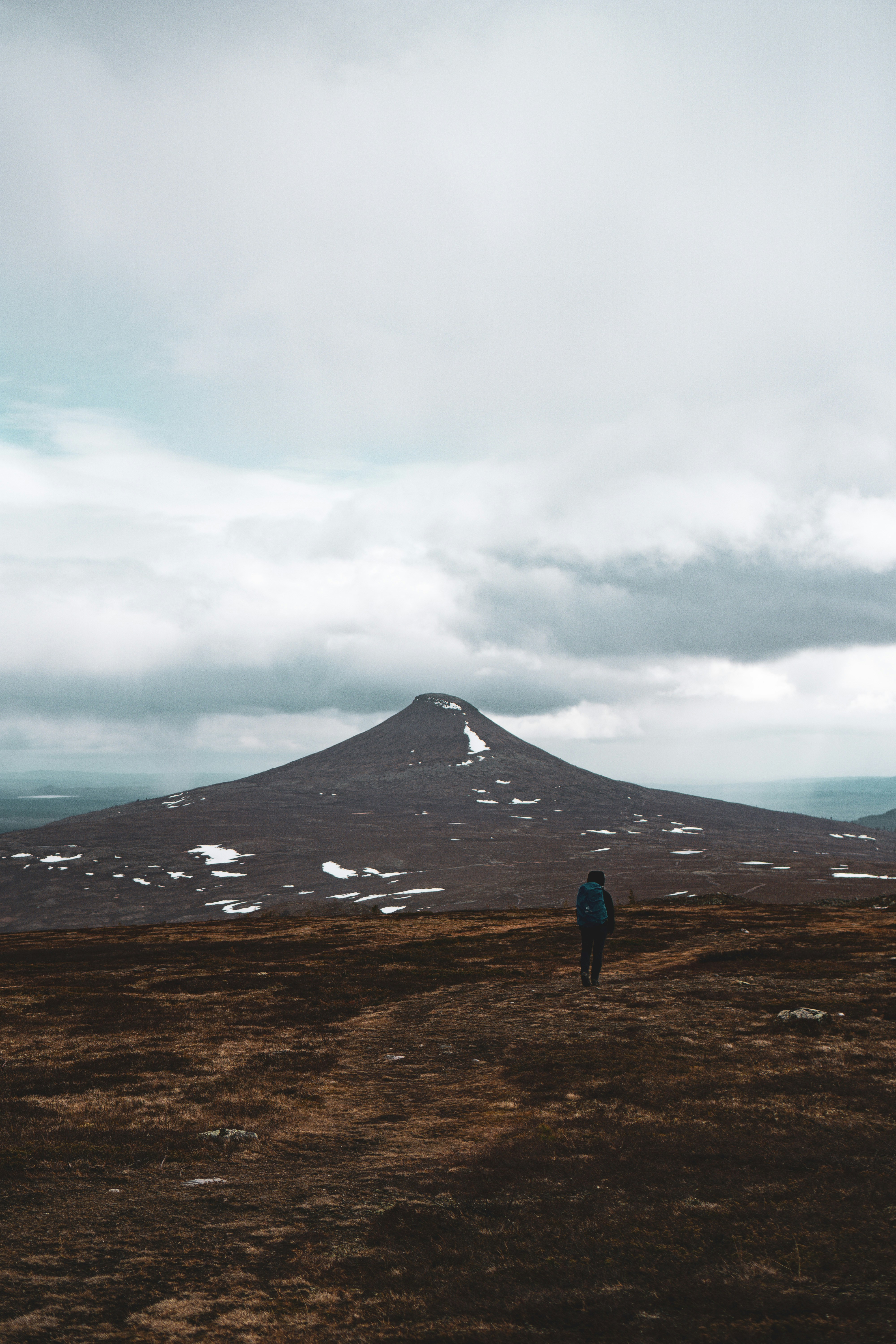 A lone hiker walks towards a conical mountain.
