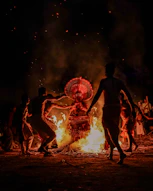 People dance around a bonfire with a performer in costume.
