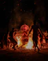 People dance around a bonfire with a performer in costume.