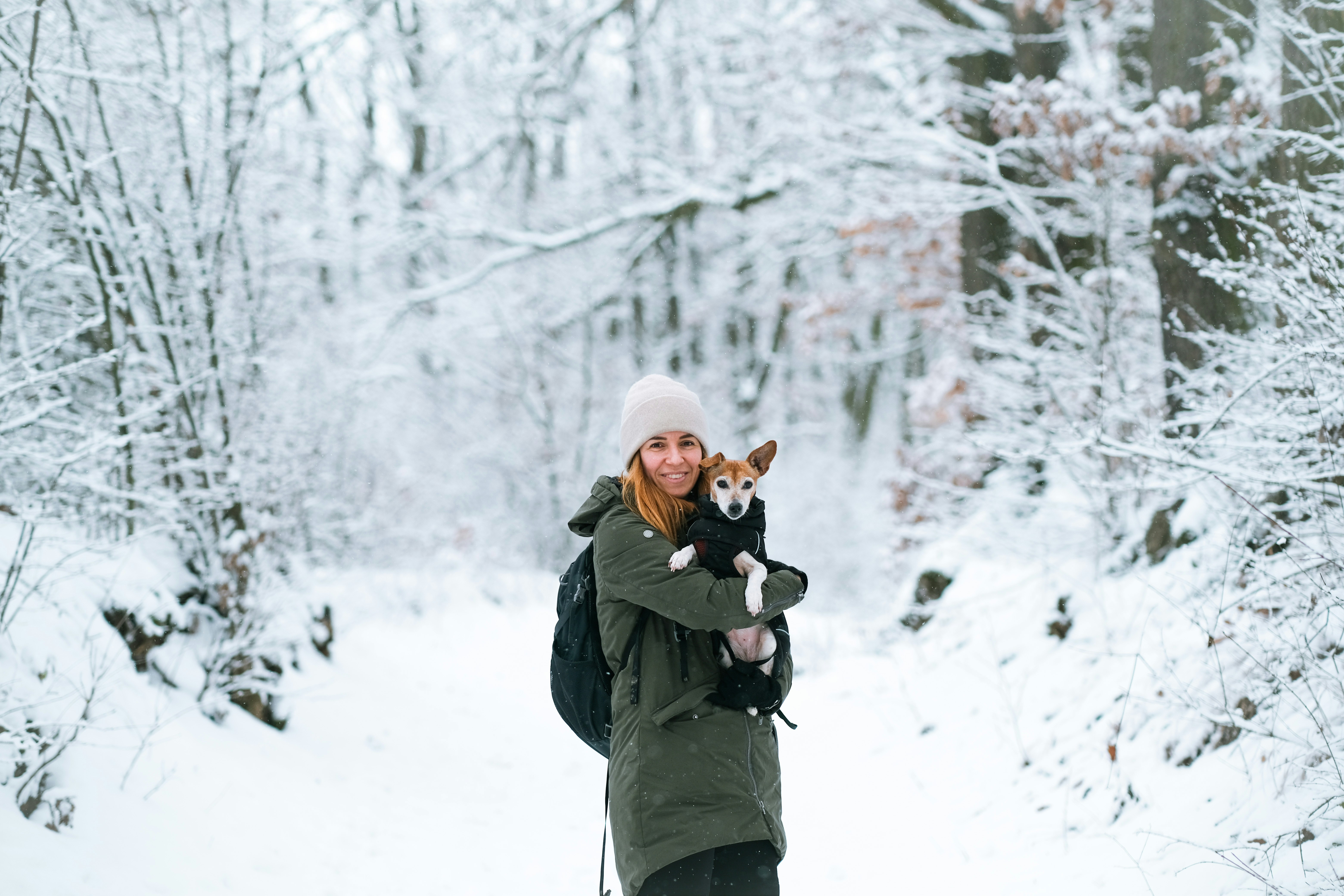 Woman holding dog in snowy forest path