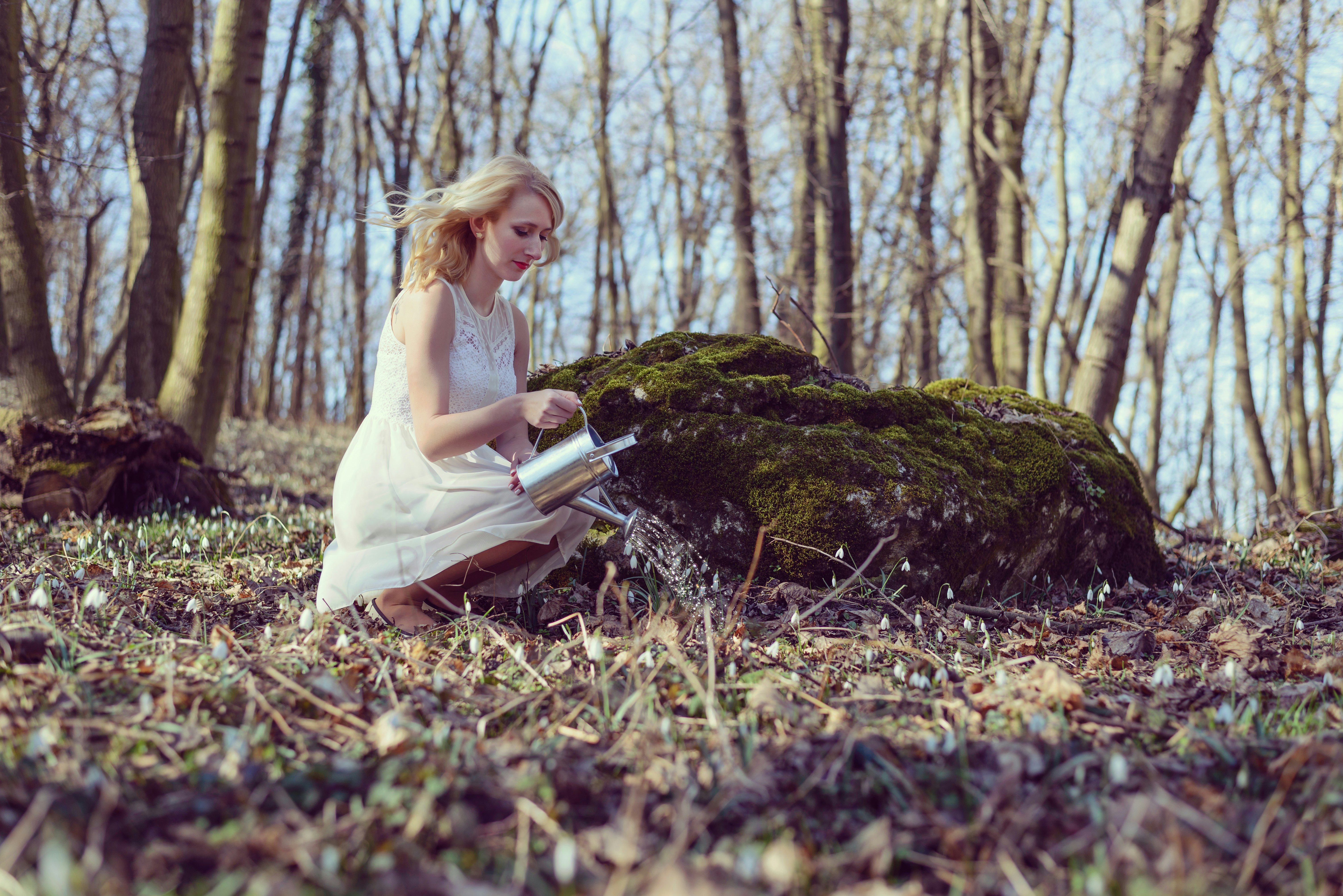 Woman watering snowdrops in a forest