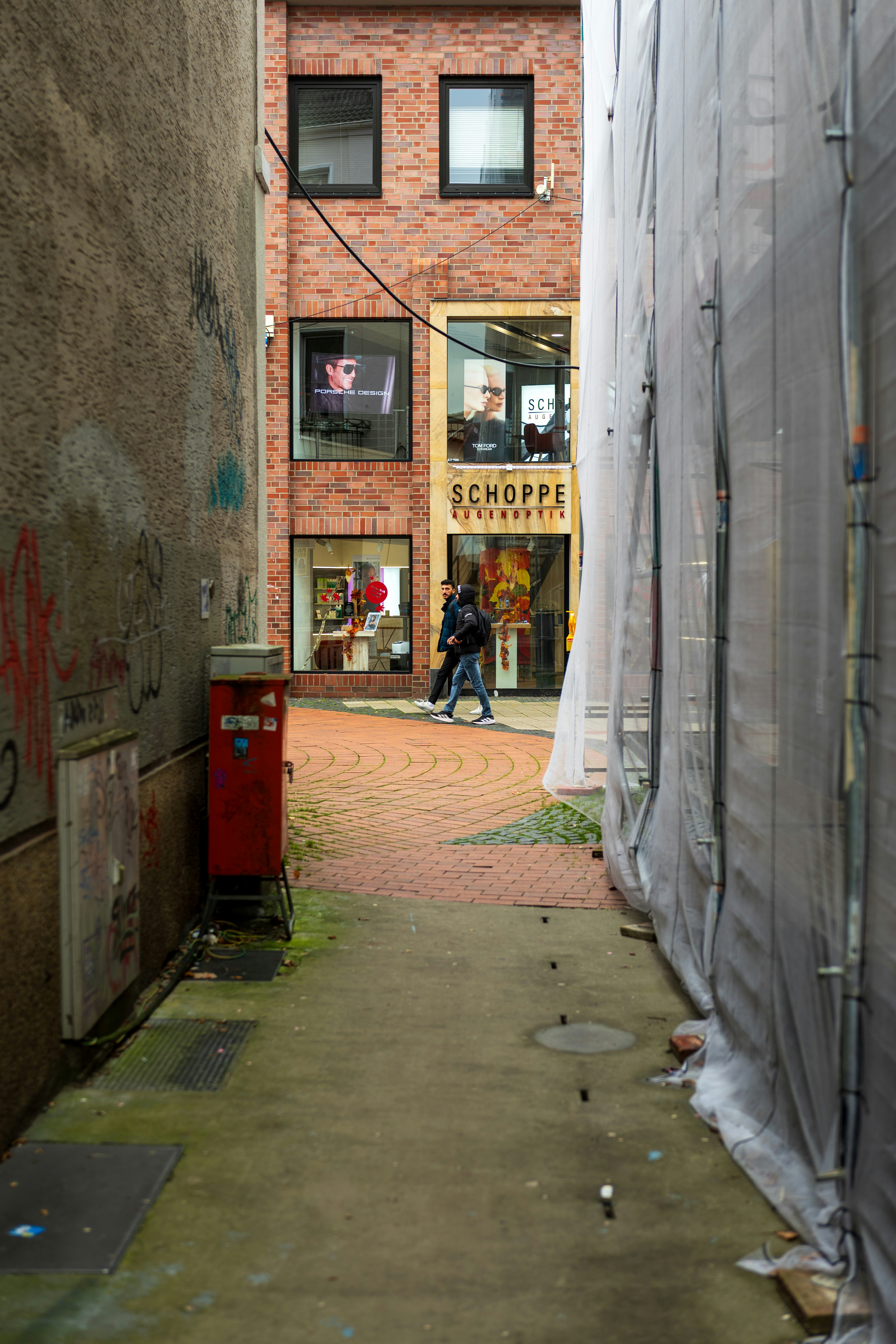 Two people walk down a narrow urban alleyway.