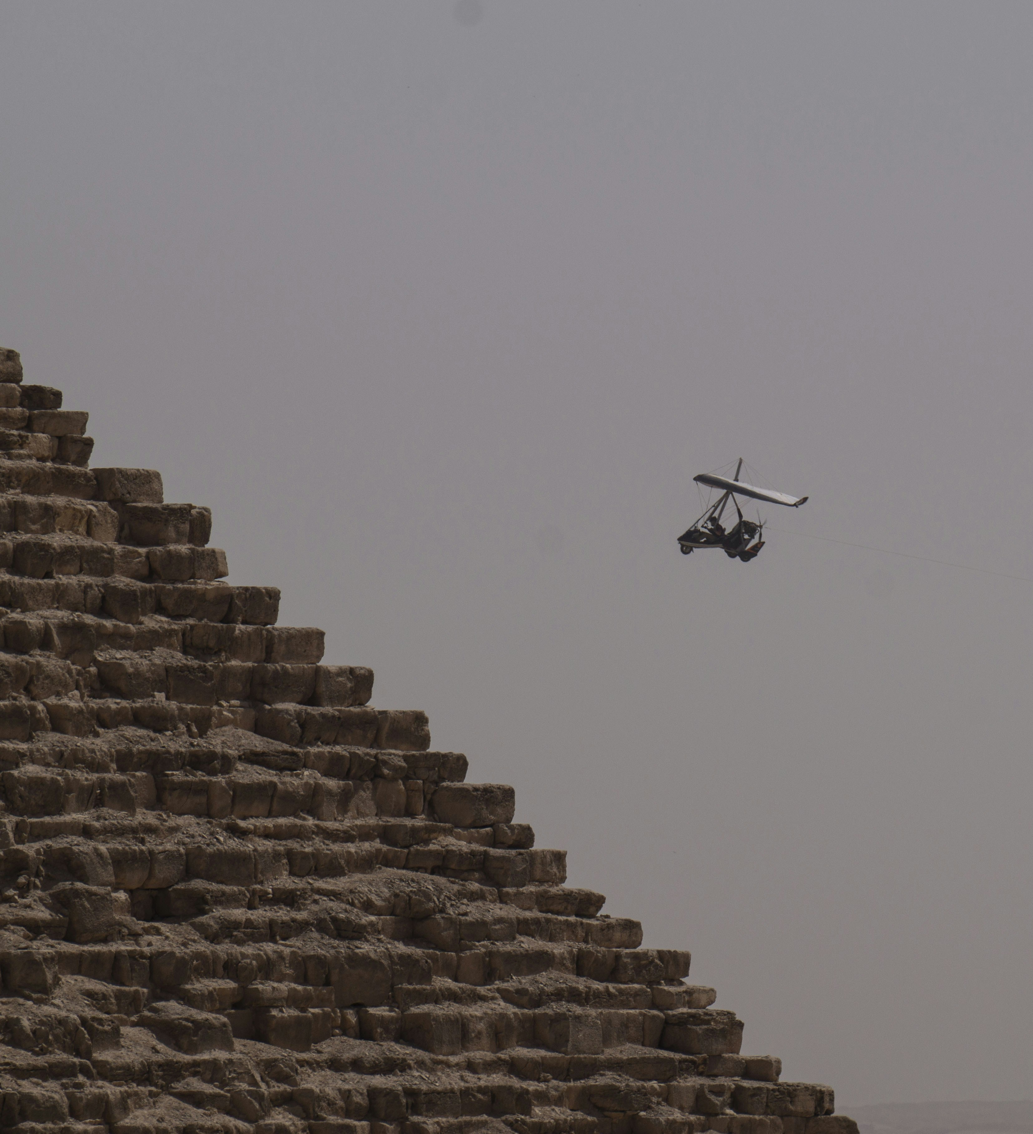 Ultralight aircraft flies near ancient egyptian pyramid.