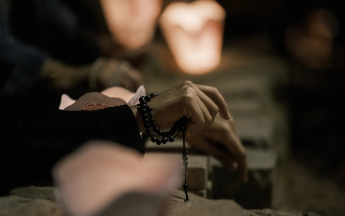 Hands holding rosary beads, lit by warm candlelight