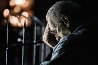 Elderly man with hand on forehead at night.
