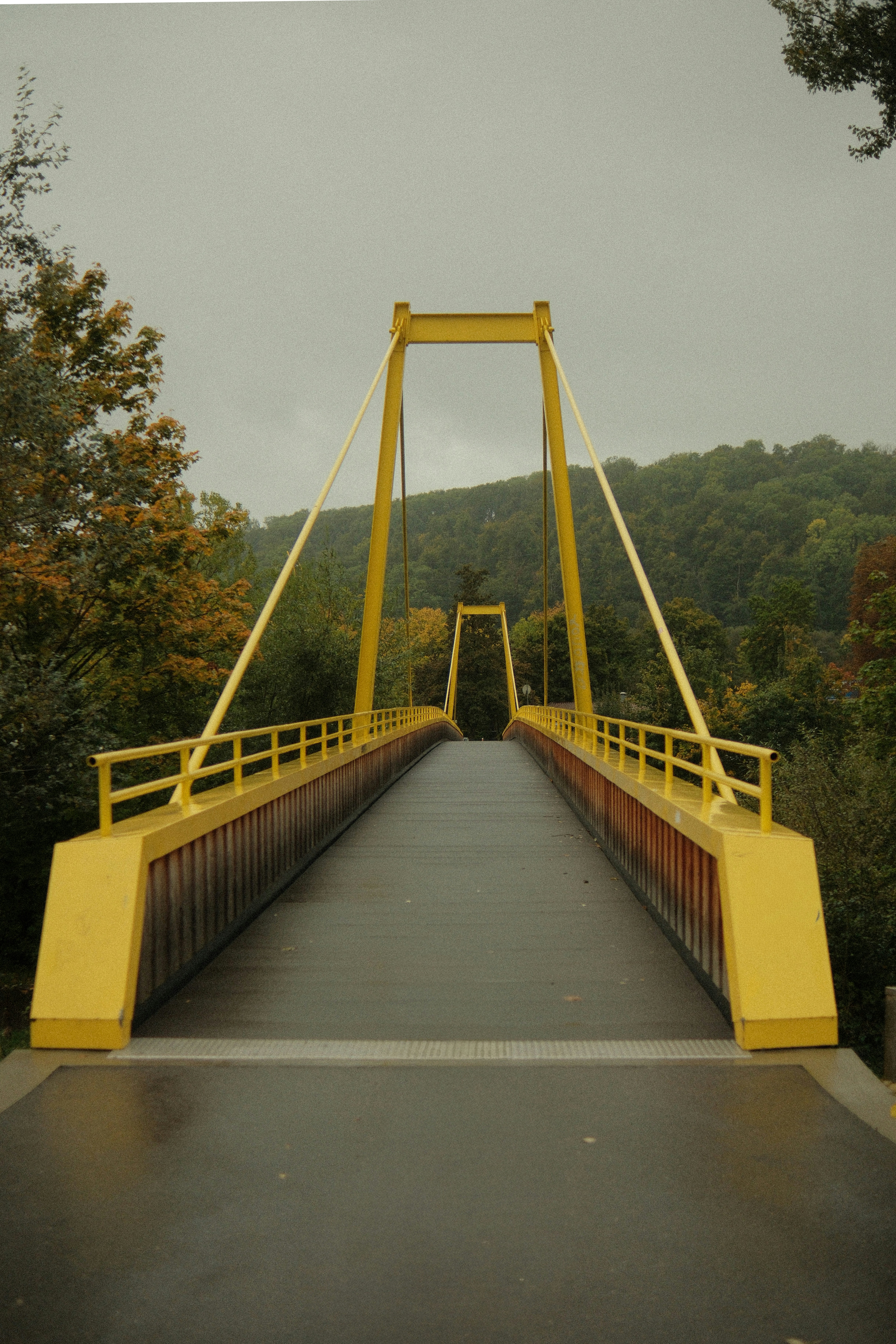 A yellow suspension bridge over a wet path.